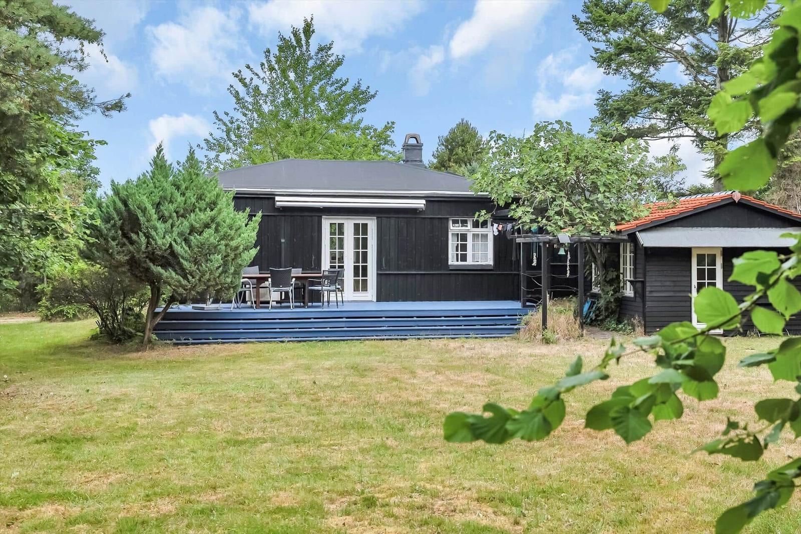 Black wooden house with terrace and garden. Table and chairs on the terrace.