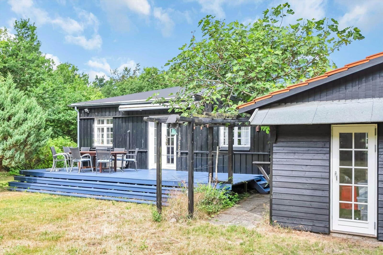 Wooden house with terrace, garden, and view of trees under blue sky.