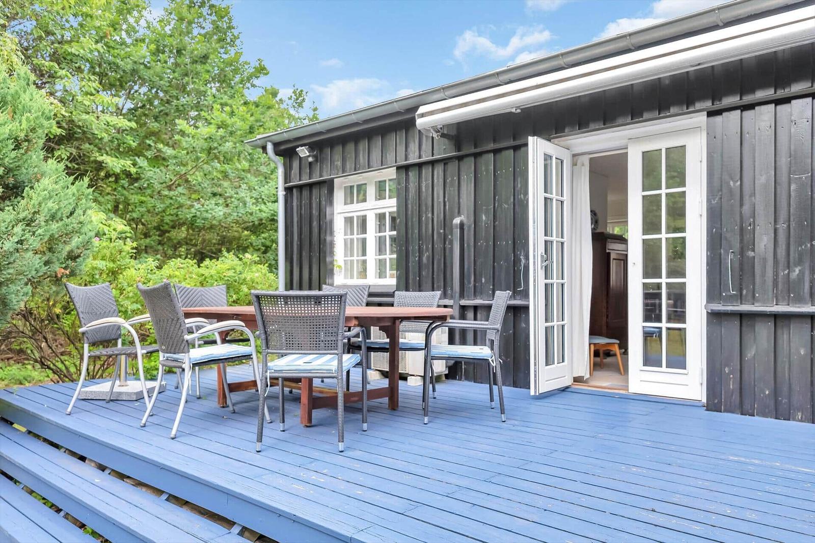 Deck with table and chairs in front of a house with white doors and dark wood.