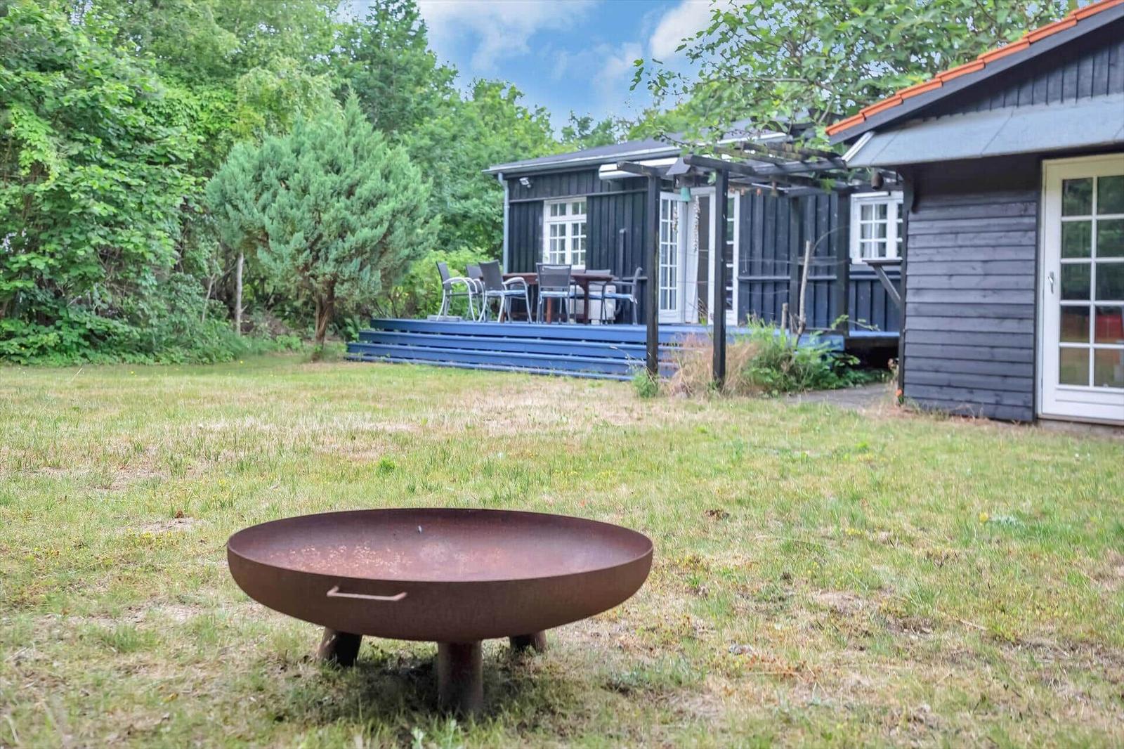 Backyard with fire pit, terrace, and garden house. Green lawn and trees surround the accommodation.