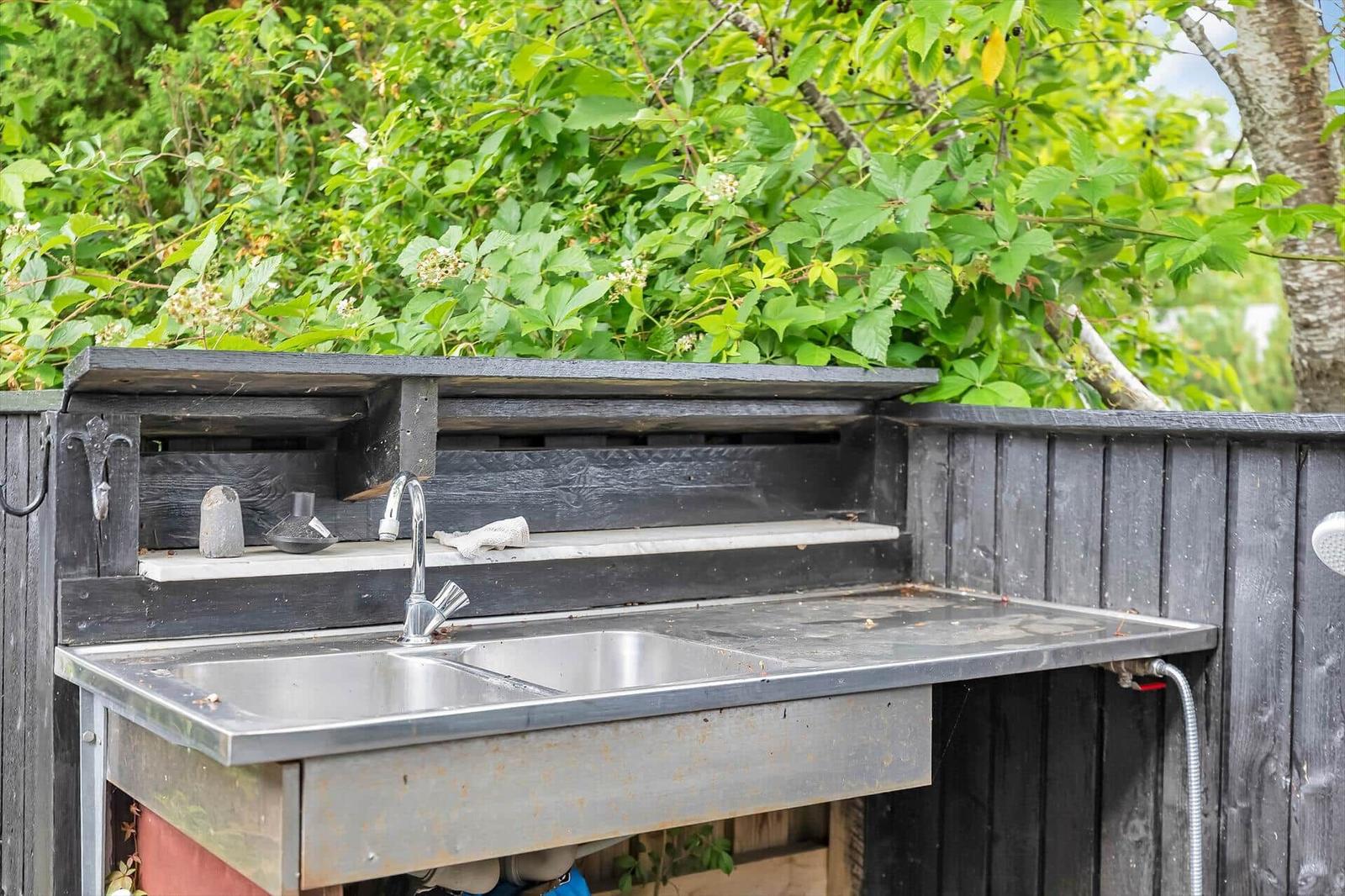 Outdoor sink with faucet and work surface on dark wooden shed