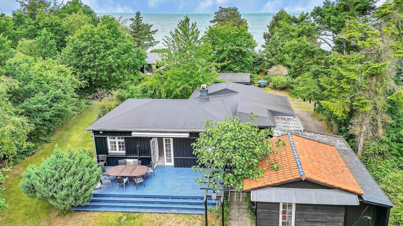 House with terrace and sea view, surrounded by trees.