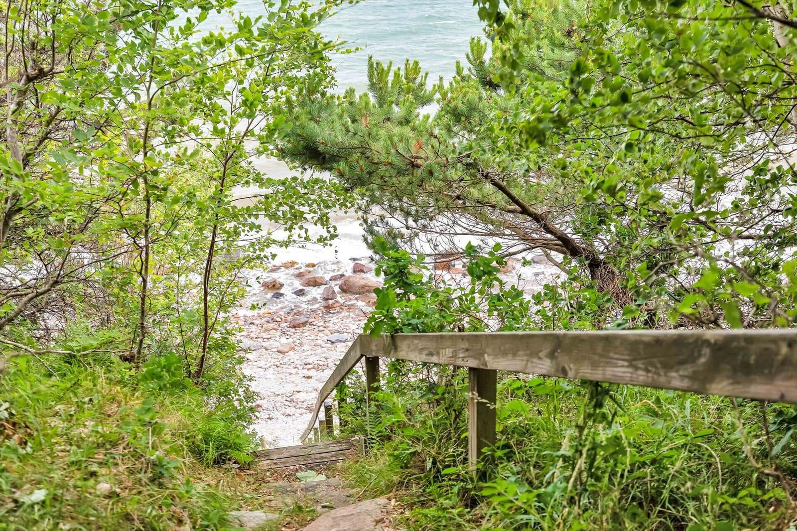 Wooden path through greenery leads to a rocky beach with the sea.
