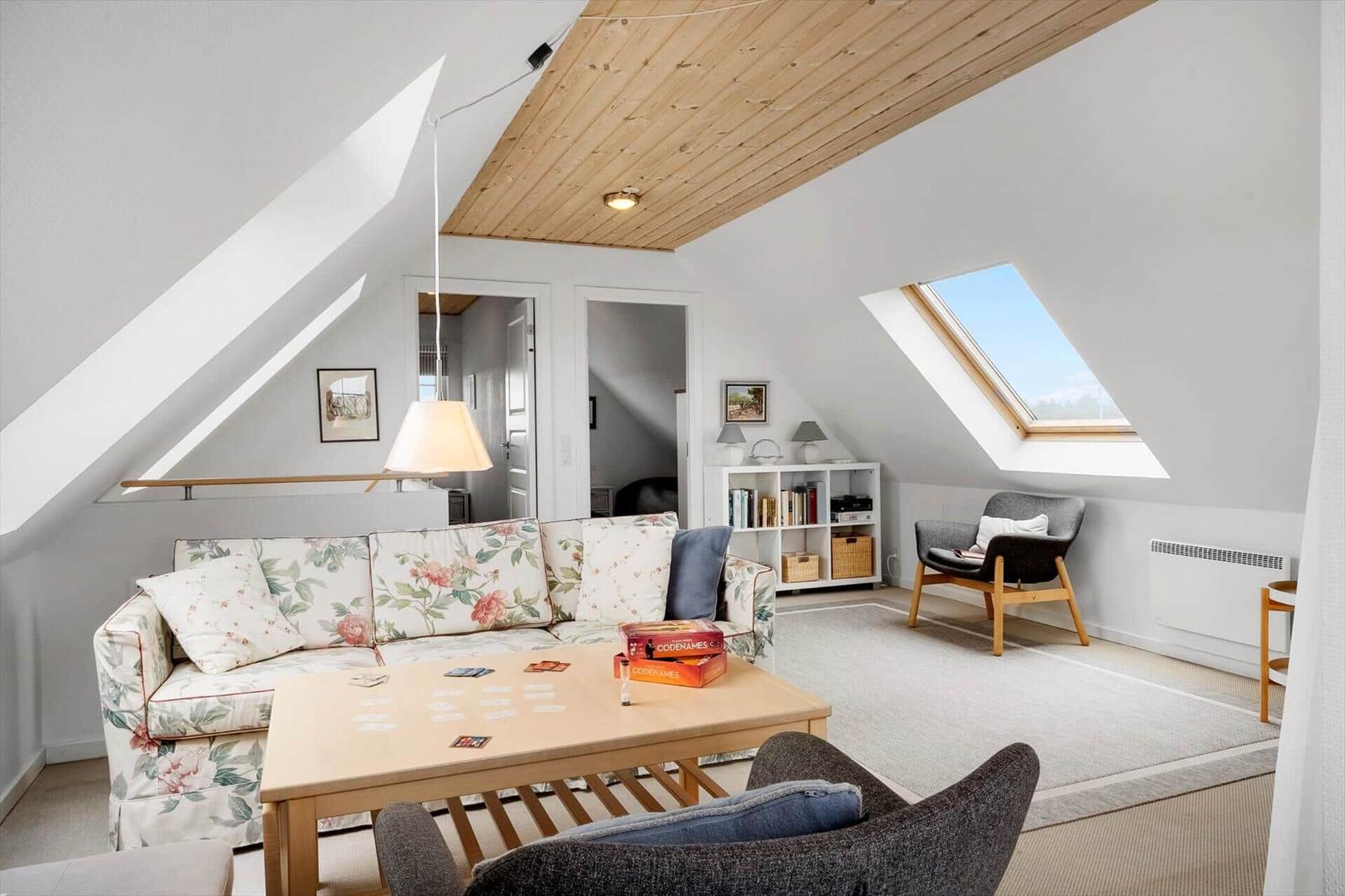 Wohnzimmer mit Sofa, Couchtisch und Sitzgelegenheiten unter Dachschrägen.