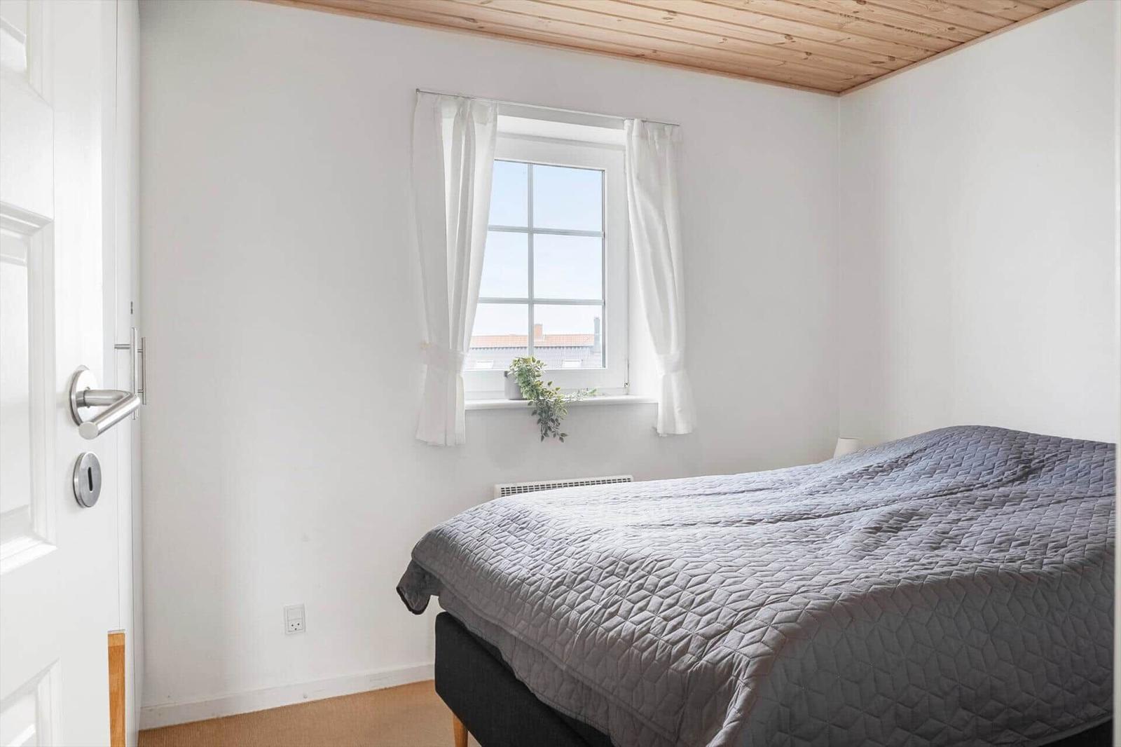 Schlafzimmer mit Bett, Fenster und Holzdecke.