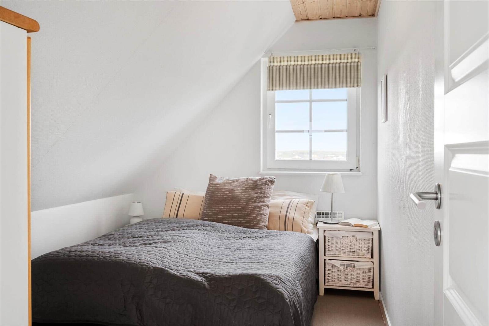 Schlafzimmer mit Bett, Nachttisch und Fenster unter Dachschrägen.