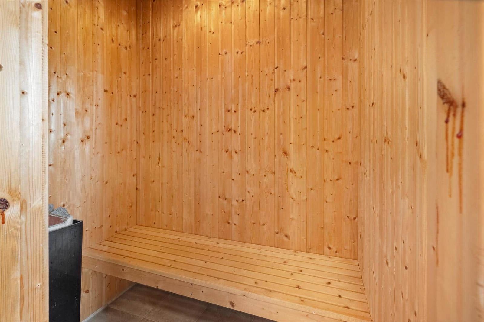 Sauna mit Holzwand und Sitzbank. Links ist ein Ofen sichtbar.