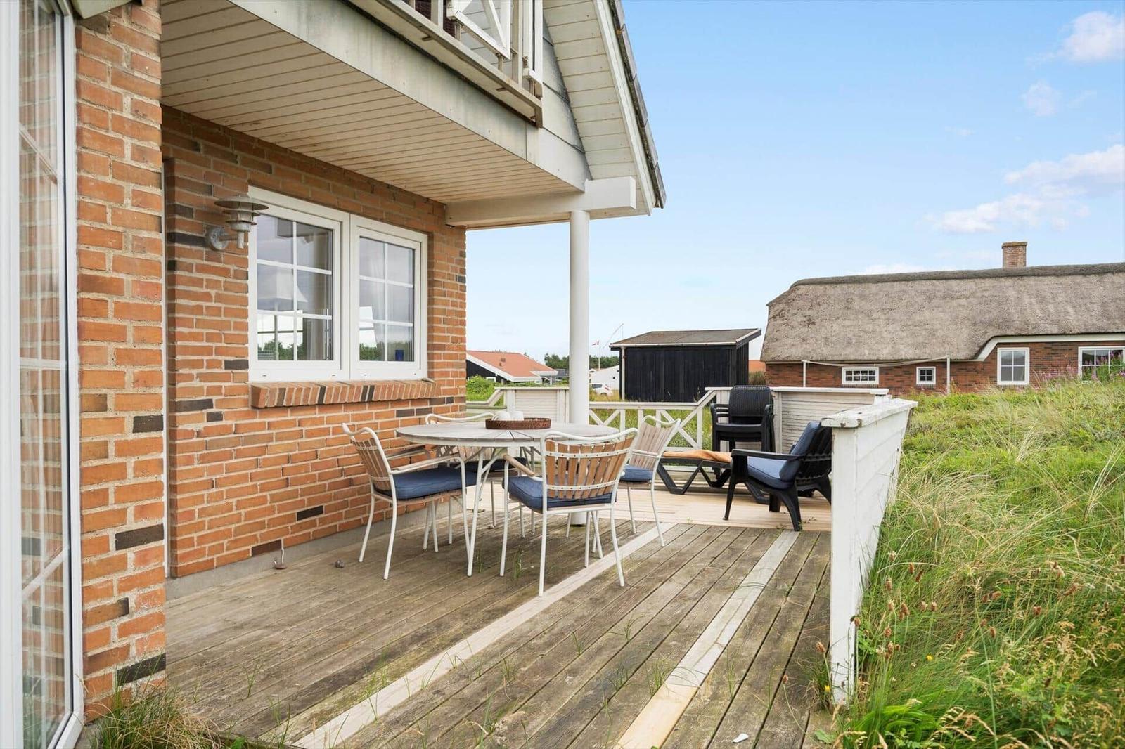 Terrasse mit Tisch und Stühlen neben einem Backsteinhaus. Im Hintergrund ist ein Dachstuhlhaus zu sehen.