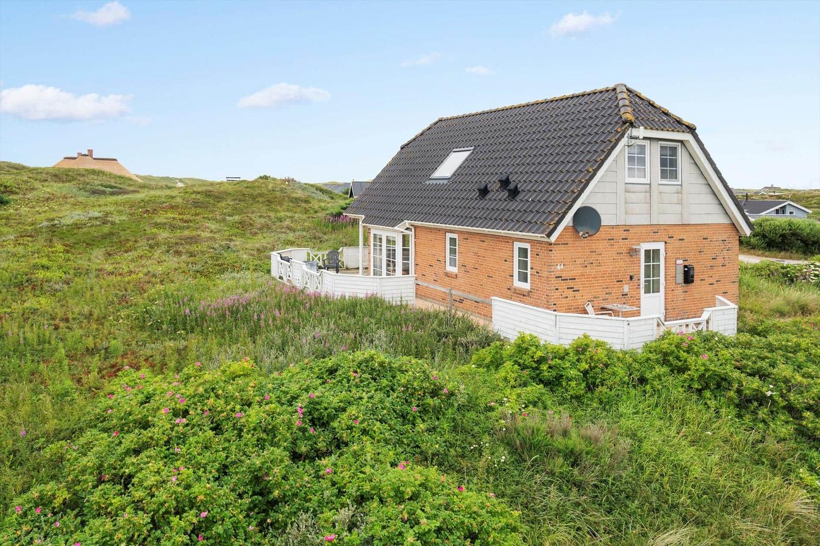 Ein Haus mit rotem Ziegelwerk und weißer Veranda liegt in einer grünen, hügeligen Landschaft.