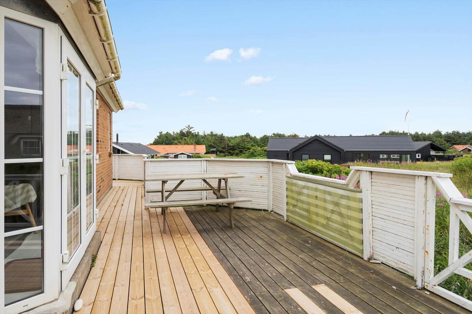 Terrasse mit Holzboden und Picknicktisch, Blick auf umliegende Häuser und Grünfläche.