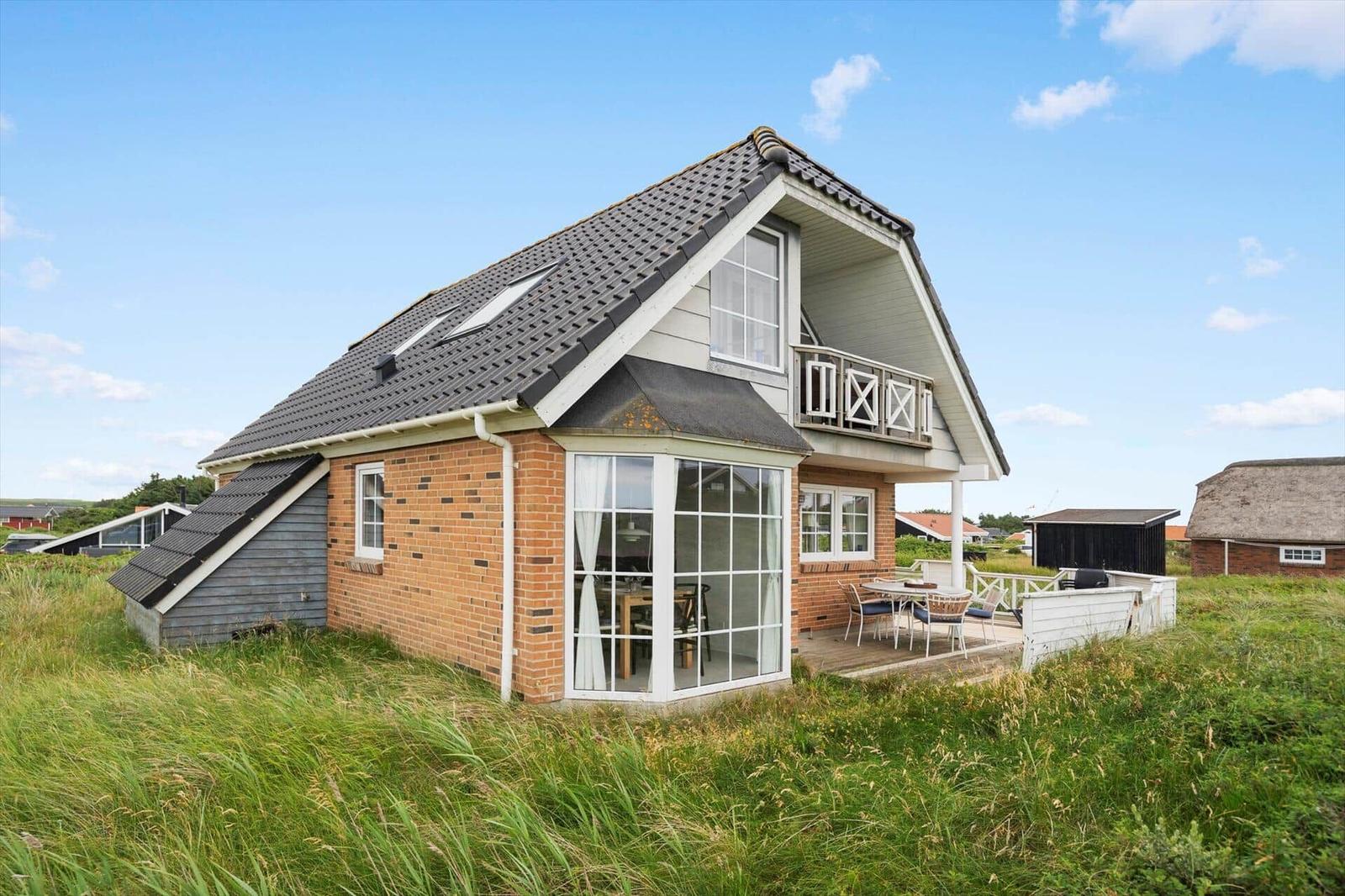 Ein Haus mit Balkon und Terrasse im Grasland unter blauem Himmel.