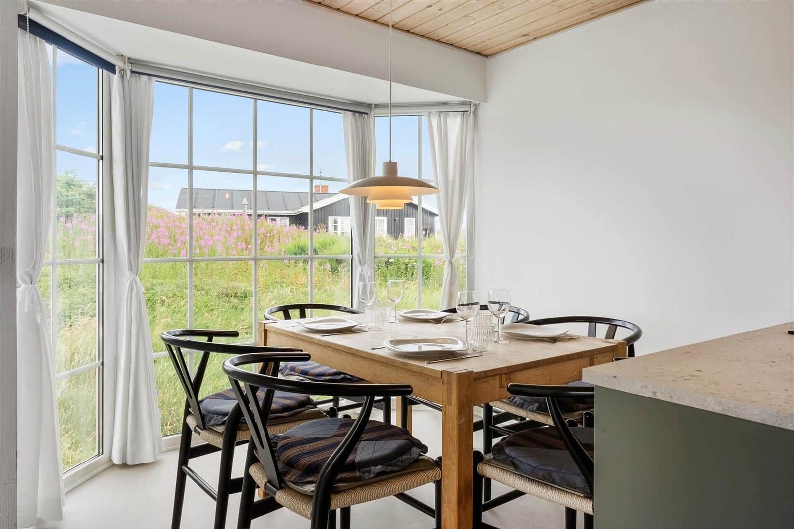 Esszimmer mit Holztisch, schwarzen Stühlen und Blick auf Felder.