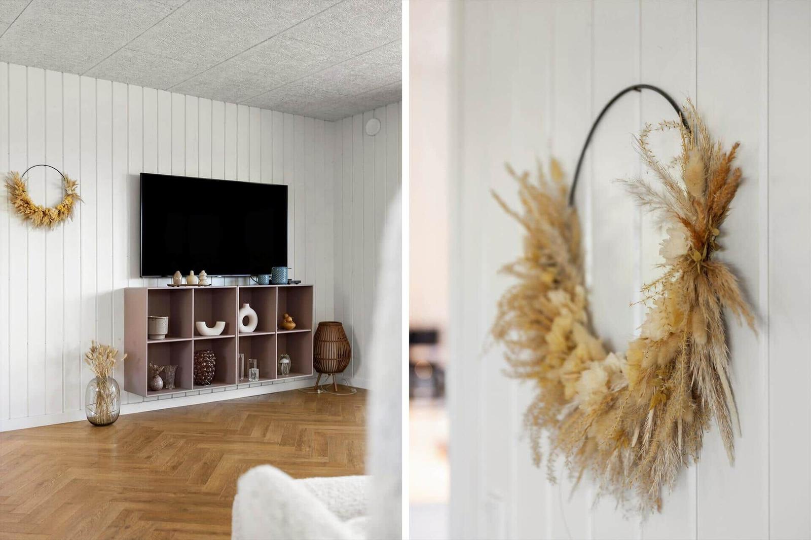 Wohnzimmer mit Fernseher, Holzboden und Trockenblumenkranz an der Wand.