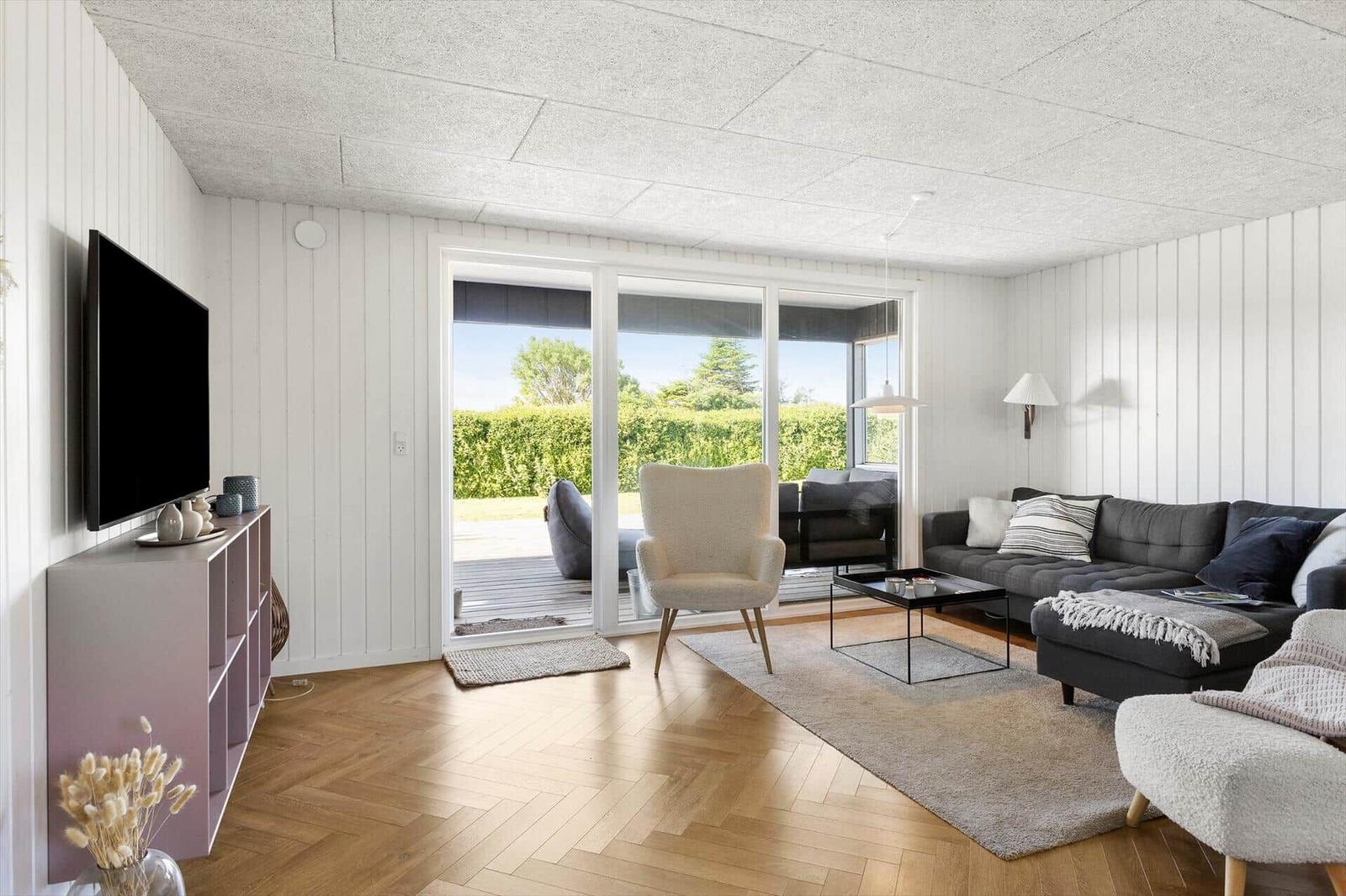 Wohnzimmer mit Sofa, Sessel und TV. Durchgang zur Terrasse mit Gartenblick.