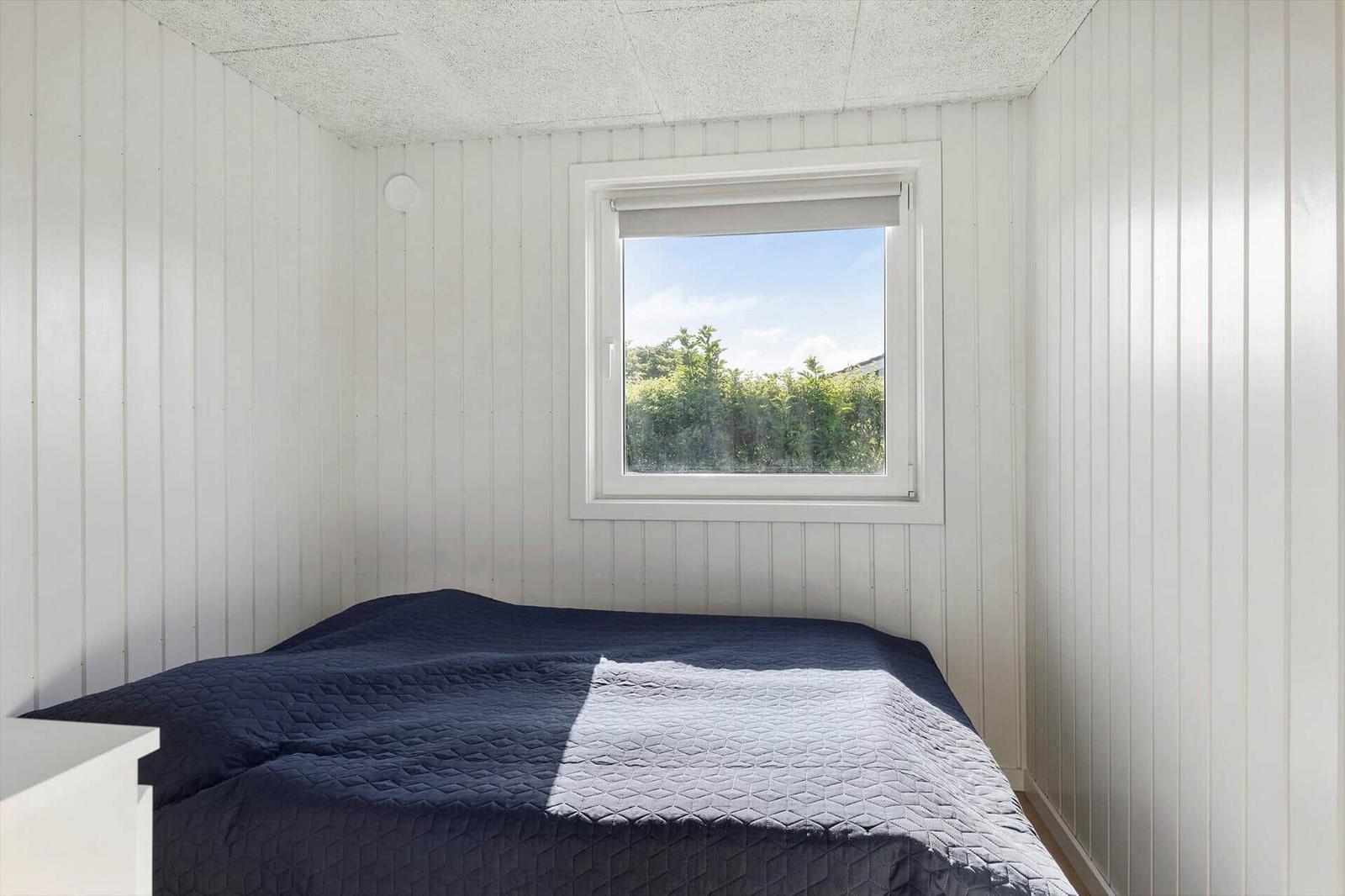 Schlafzimmer mit Bett, Fenster und weißen Wänden.