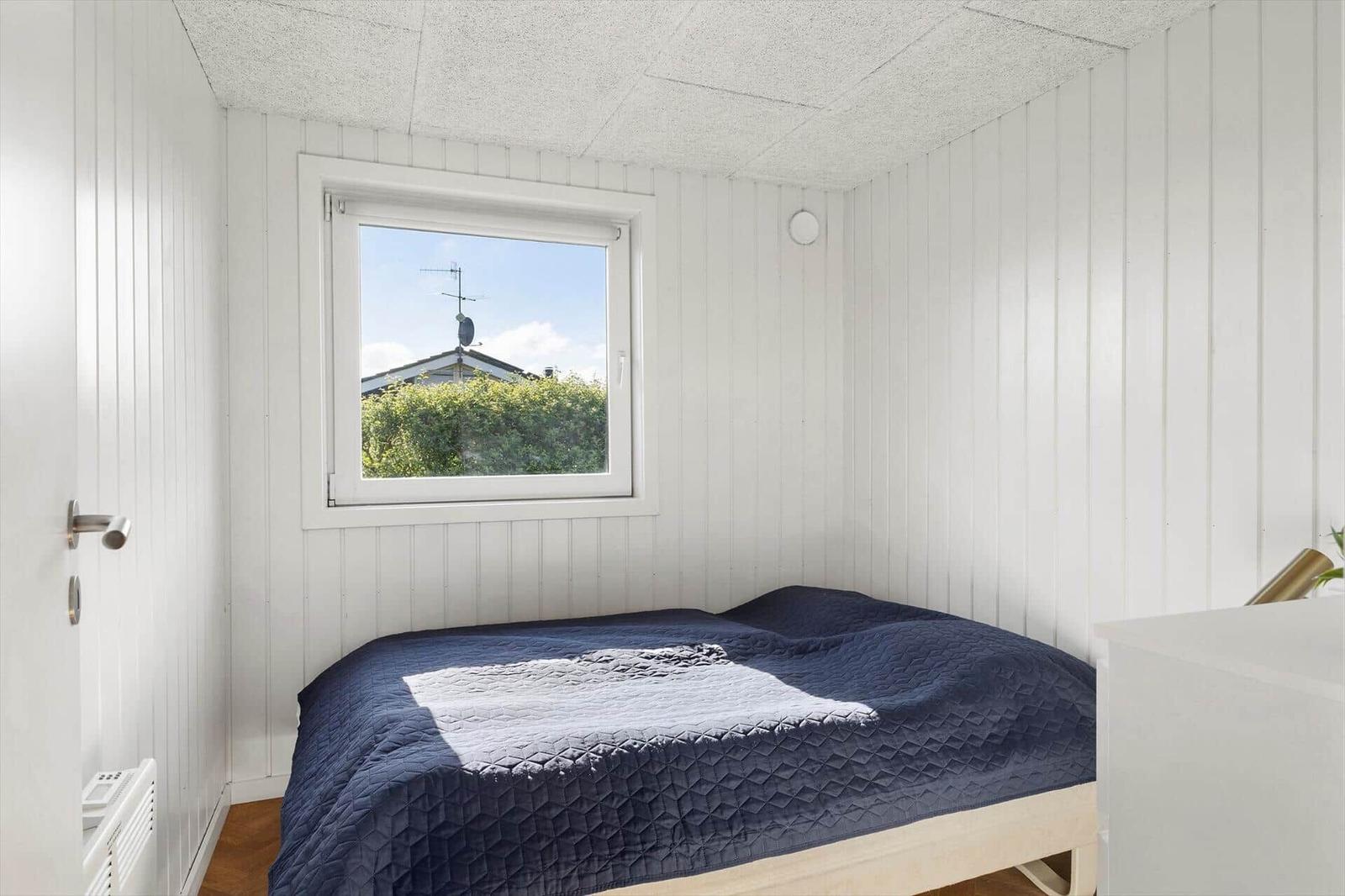 Schlafzimmer mit Bett, Fenster und weißen Wänden.