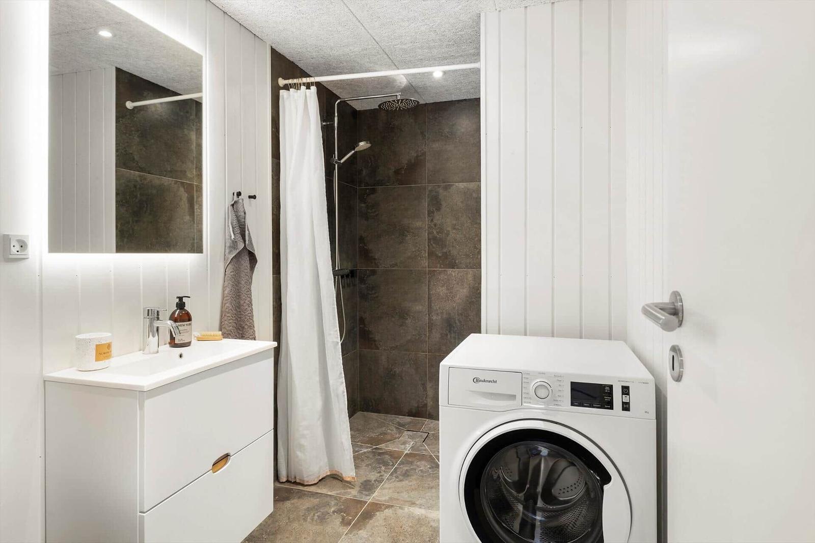 Badezimmer mit Dusche, Waschmaschine und Spiegelschrank.