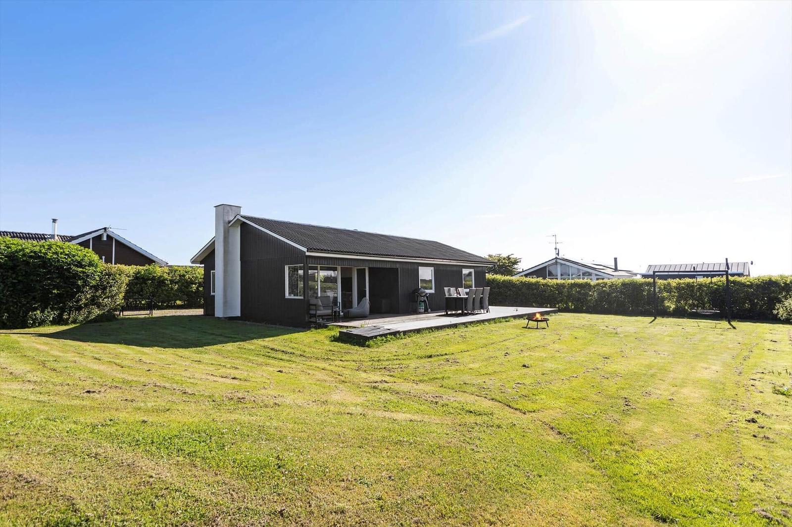 Ein Haus mit Terrasse, Garten und Feuerkorb unter blauem Himmel.