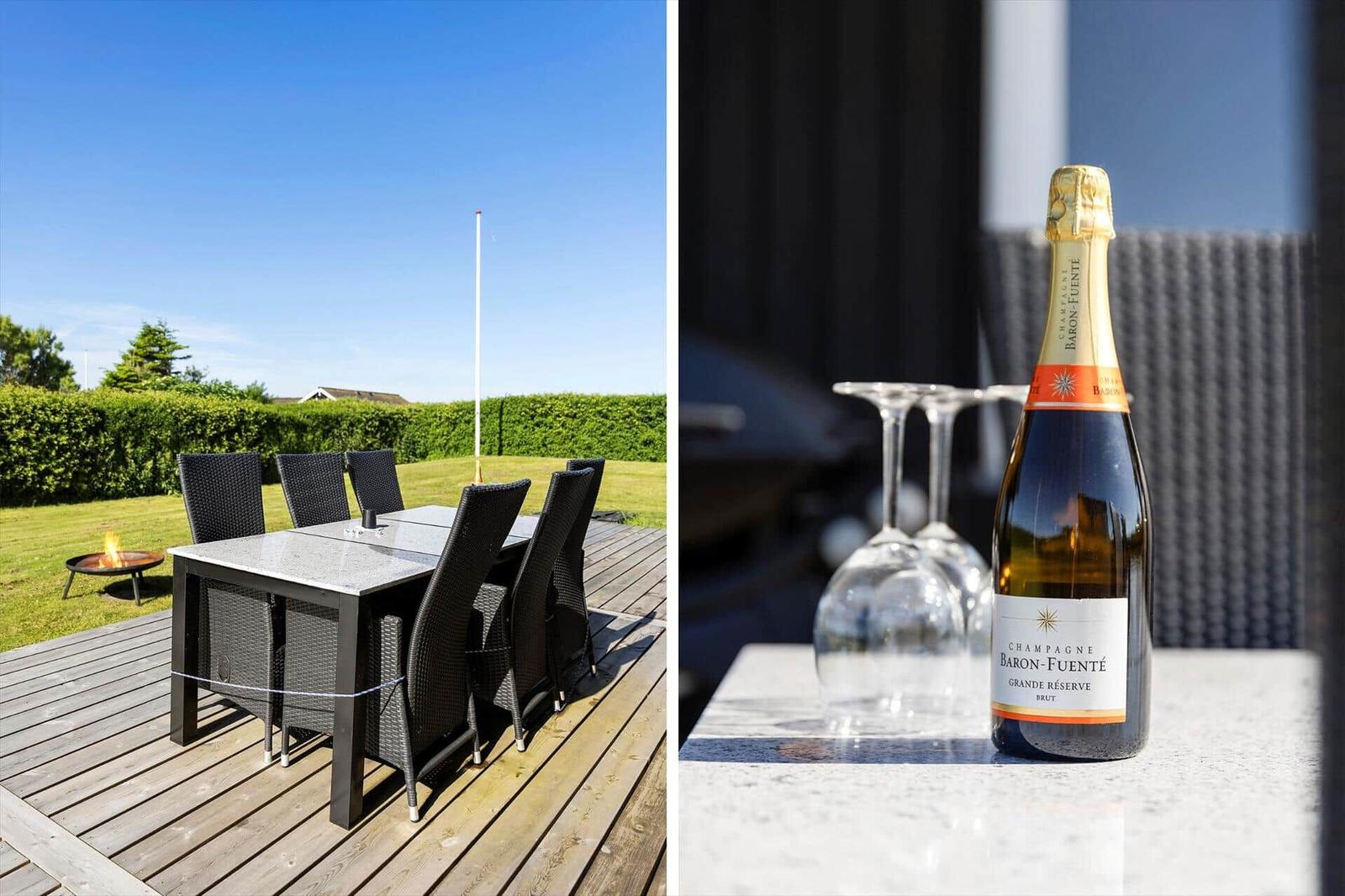 Außenbereich mit Tisch und Stühlen, Grill und Feuerkorb. Flasche Champagner und Gläser auf Tisch.