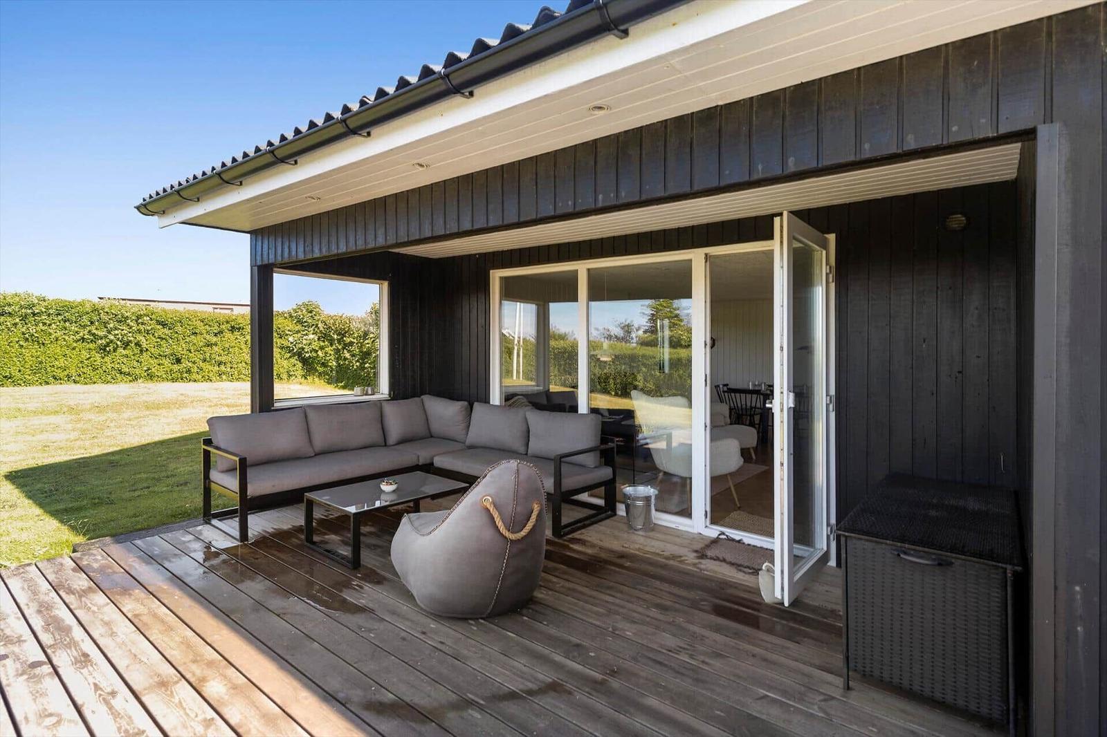 Terrasse mit Sofa, Tisch und Sessel. Durchgehende Glasschiebetüren führen ins Haus.