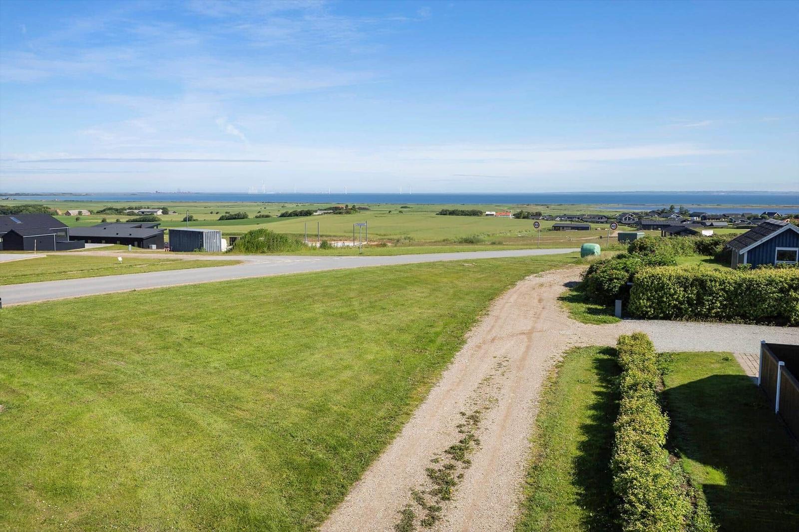 Weitläufiger Blick auf Grünflächen, Straßen und das Meer mit Windkraftanlagen im Hintergrund.
