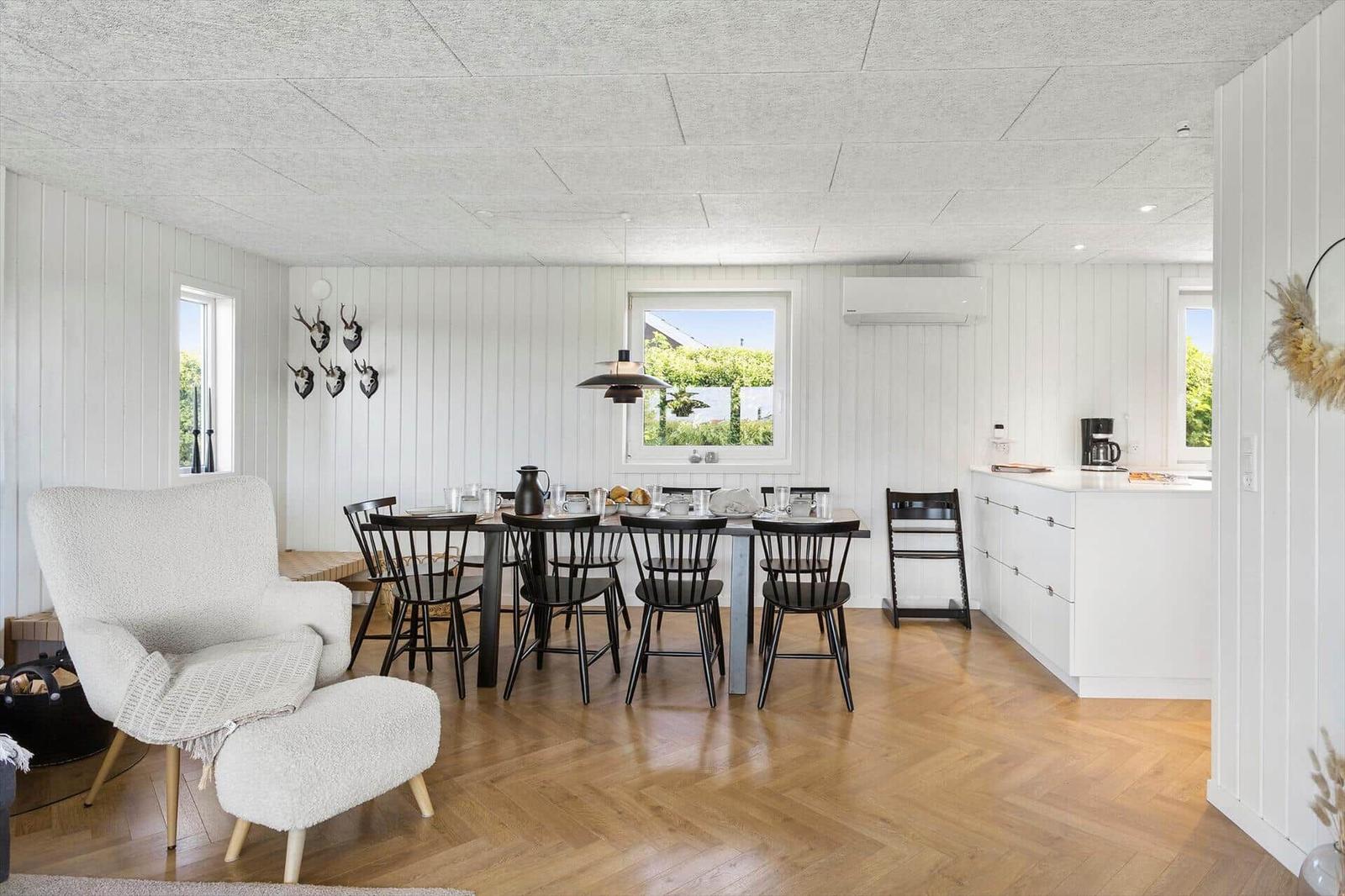 Essbereich mit Tisch, Stühlen und Küchenzeile. Helle Wände, Holzboden und Fenster.
