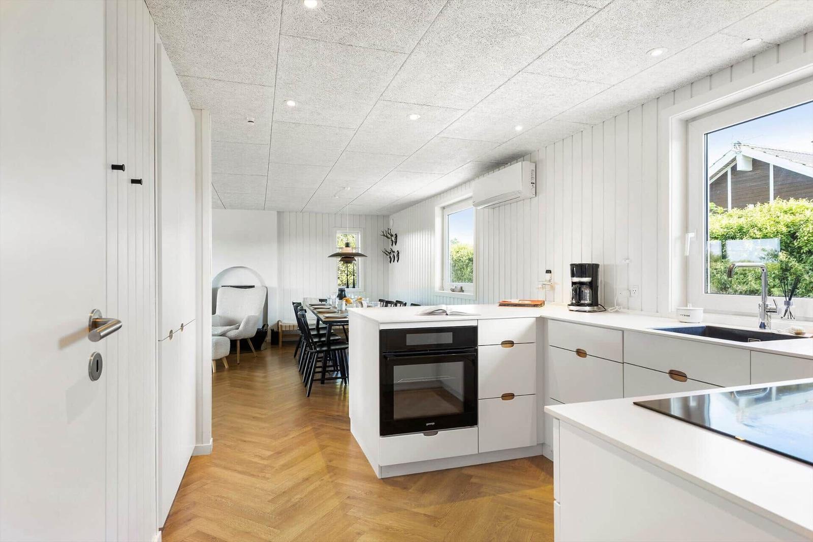 Küche mit weißer Arbeitsplatte, Dunstabzug und Fenster. Hinterher Essbereich mit Tisch und Stühlen.