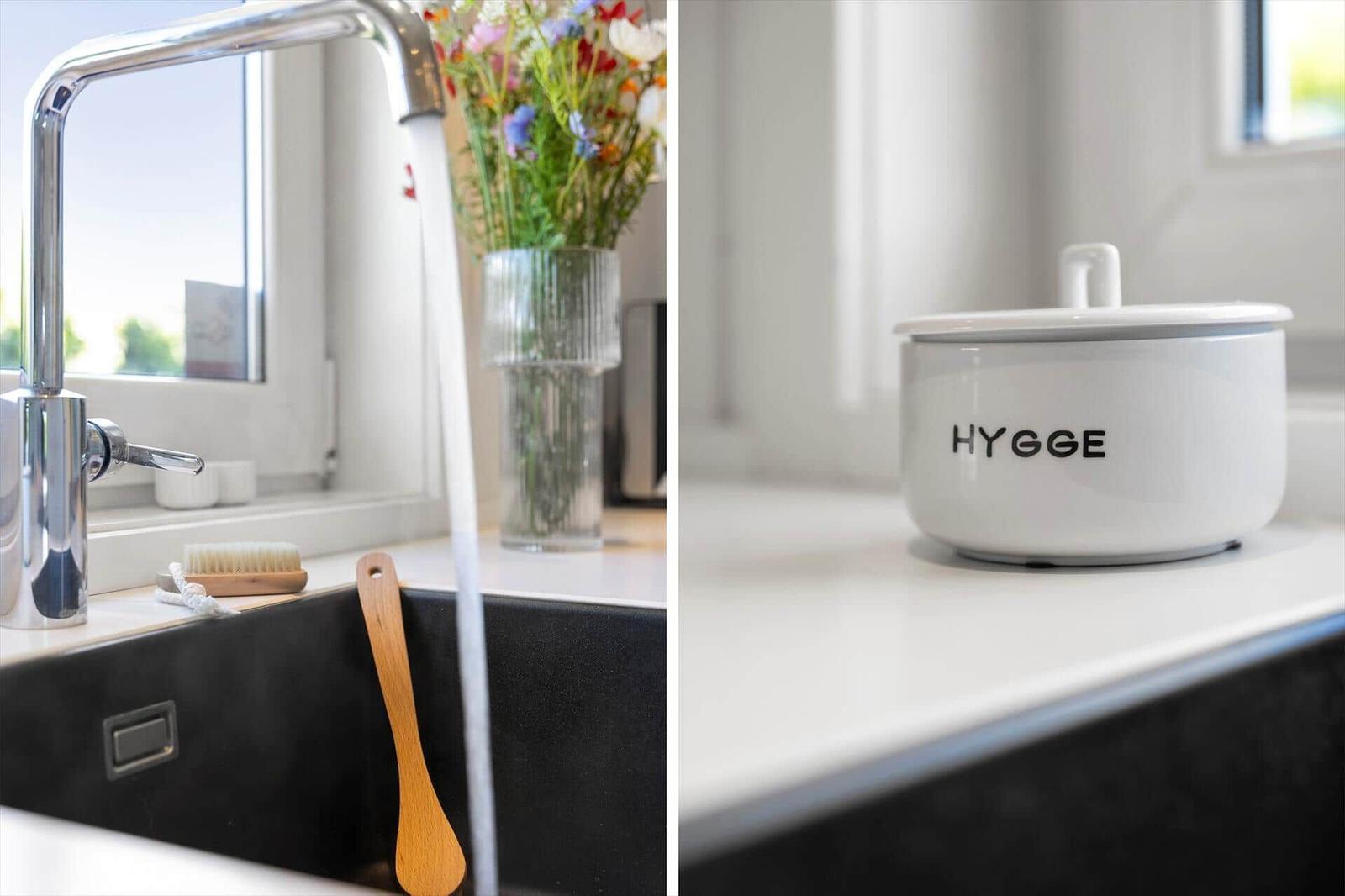 Küchenbereich mit Wasserhahn, Blumen und Schüssel mit Aufschrift HYGGE