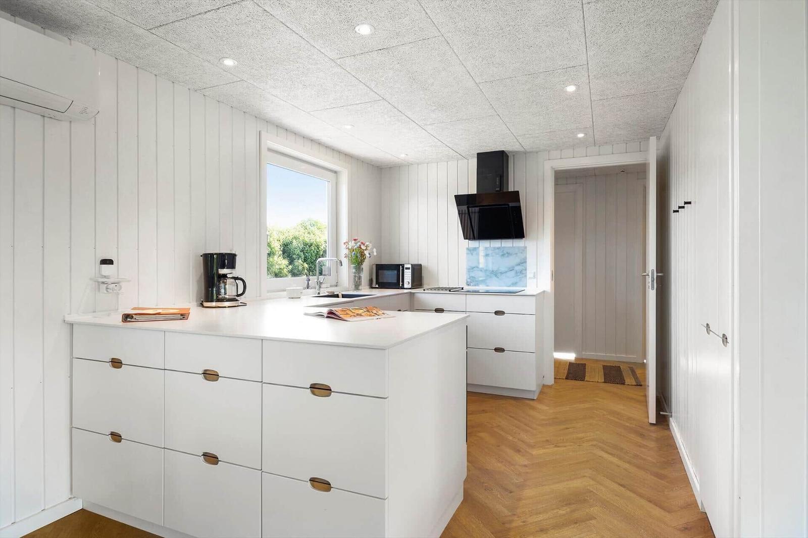 Küche mit weißer Arbeitsplatte, Holzboden und Fenster mit Blick auf Grün.