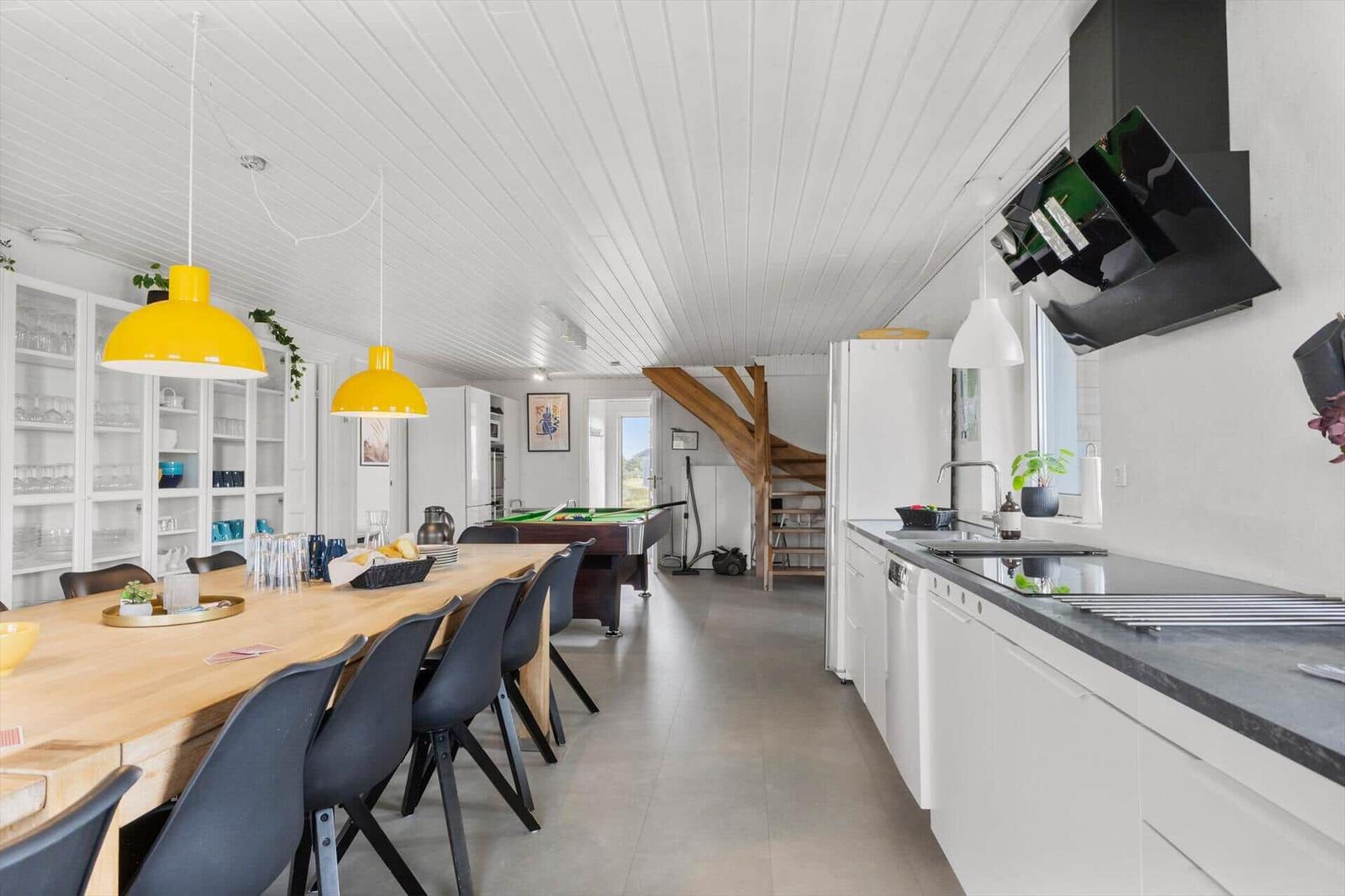 Kitchen with dining area and pool table. White furniture, yellow lamps, wooden table.