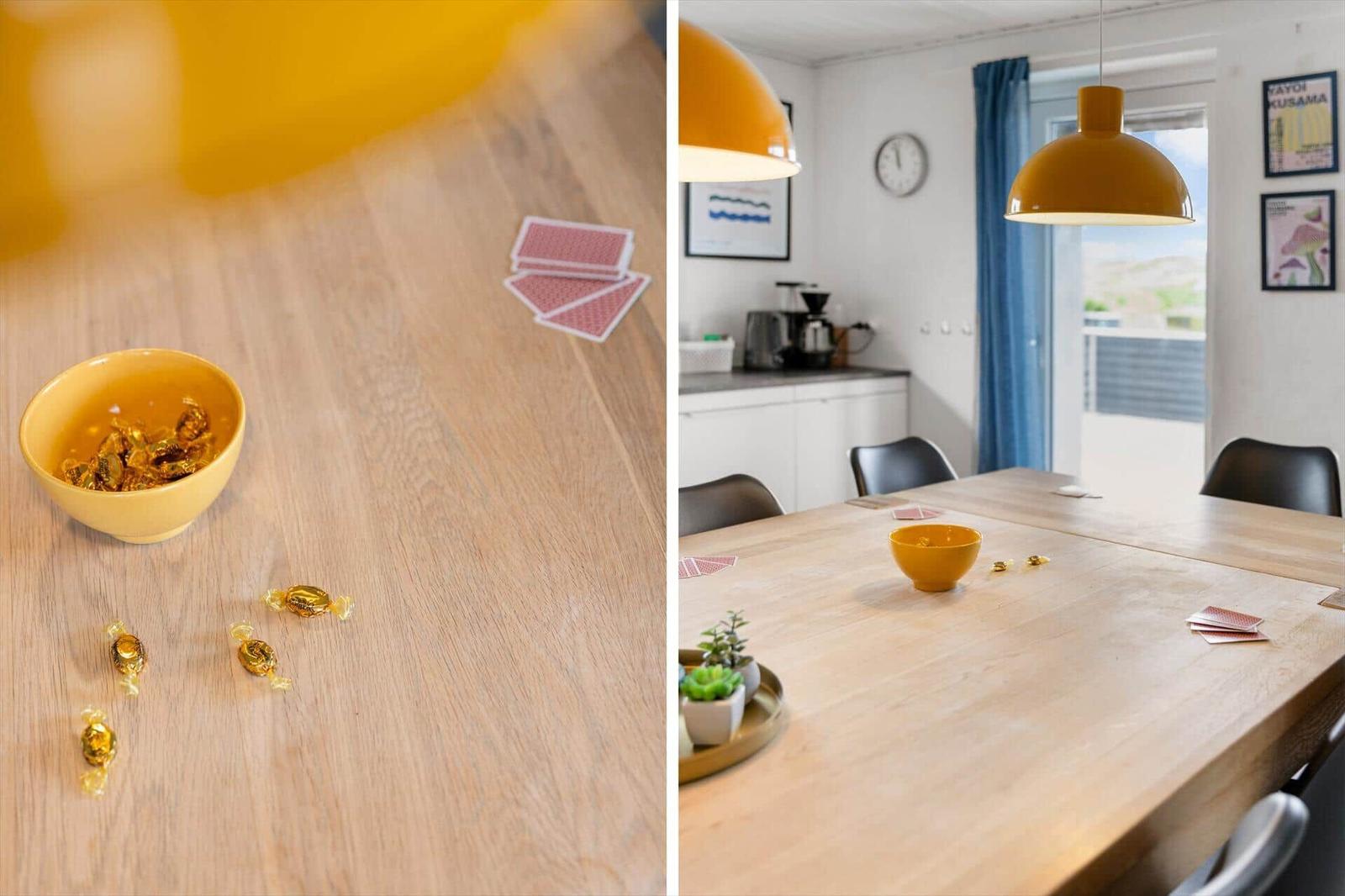 Wooden table with yellow bowl, candies, and cards. Background: kitchen and window.