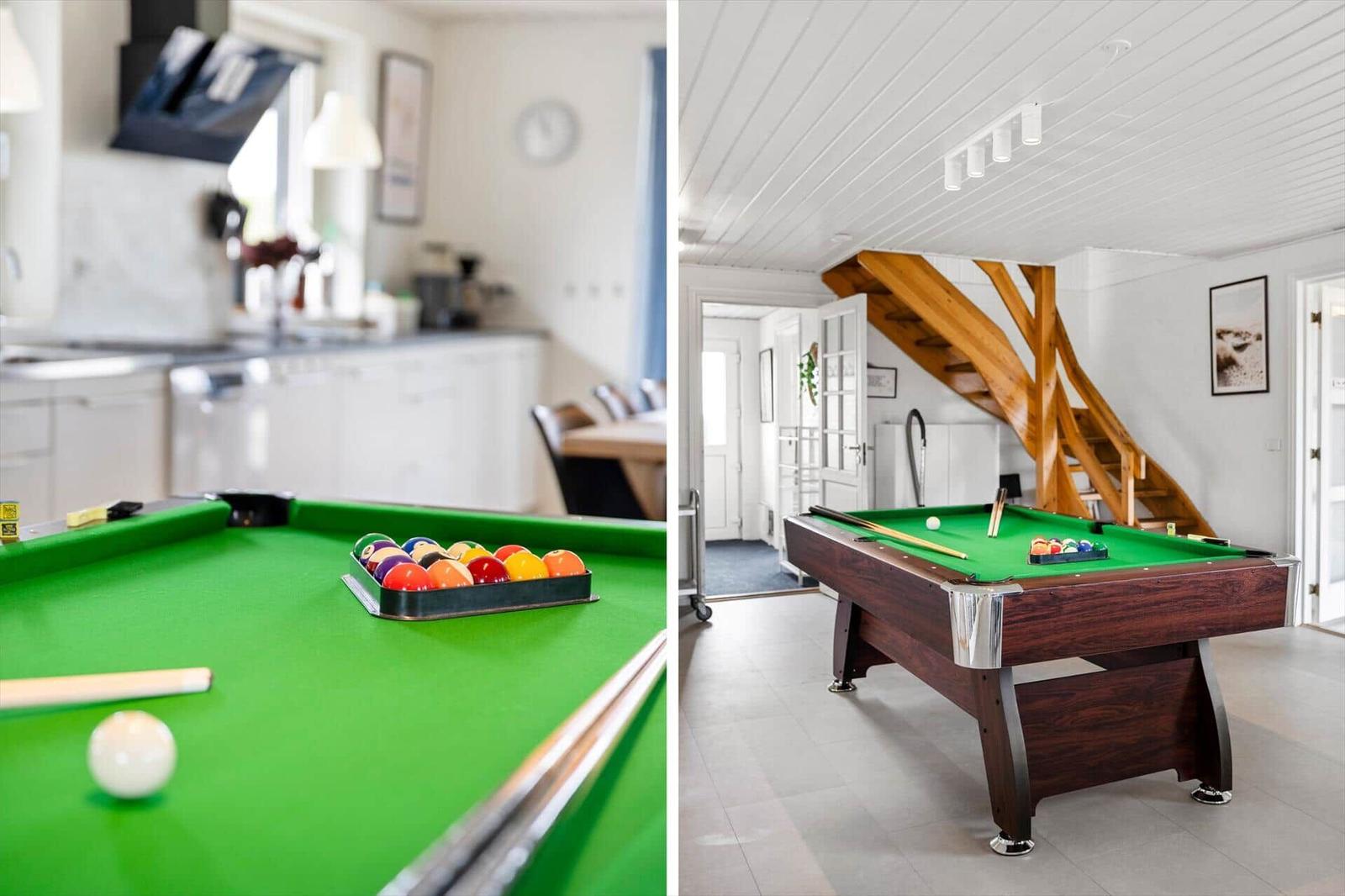 Billiard table with balls and cue in a bright room with kitchen area in the background.