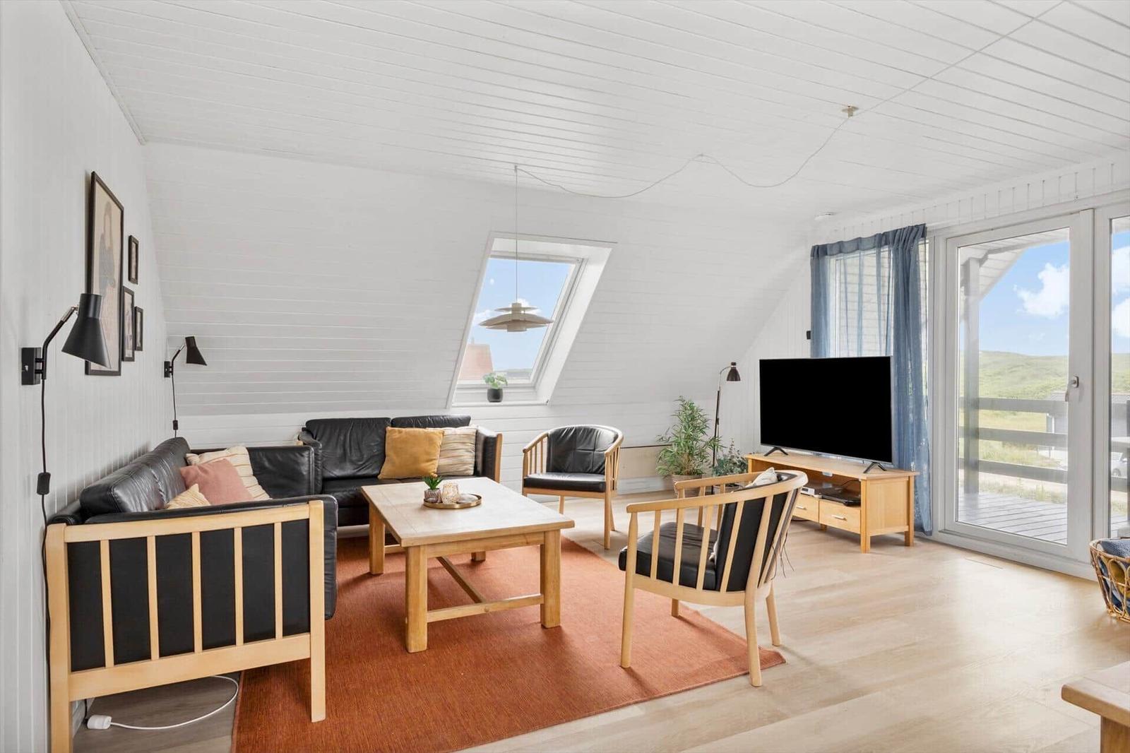 Living room with sofa, chairs, coffee table, and TV. Large windows and door to a terrace.