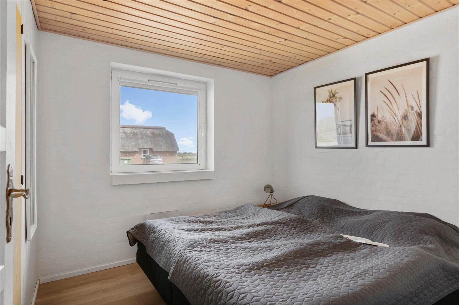 Bedroom with bed, window, and wooden ceiling. Two pictures hang on the wall.