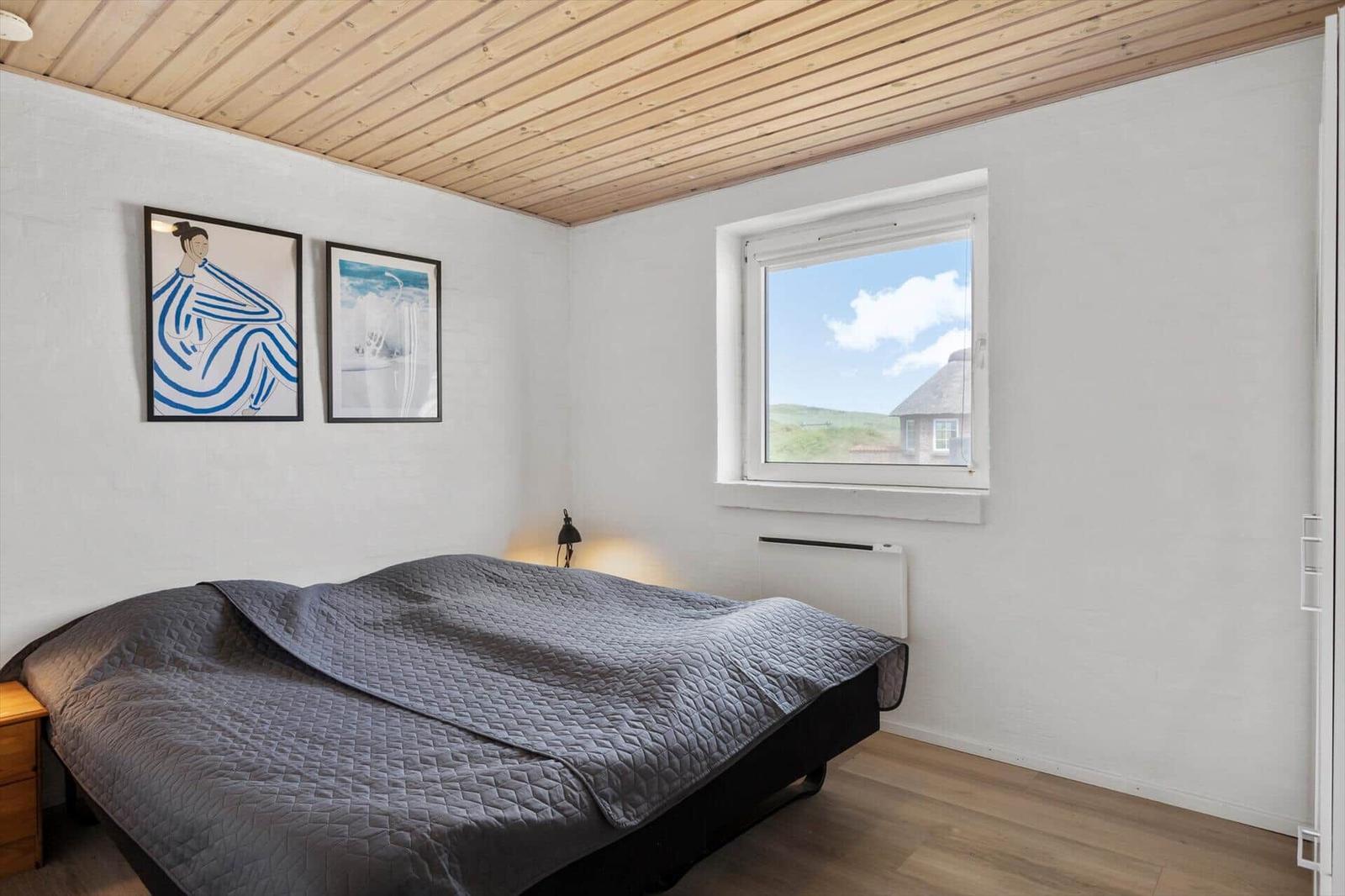 Bedroom with bed, window, and two pictures on the wall.