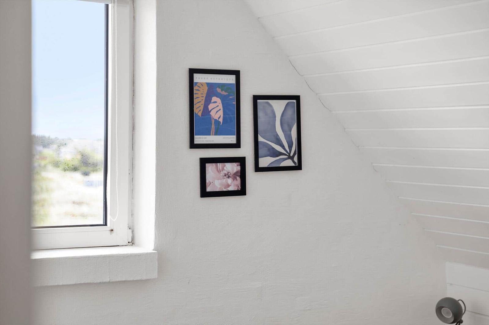 Three framed pictures on a white wall under a skylight window.