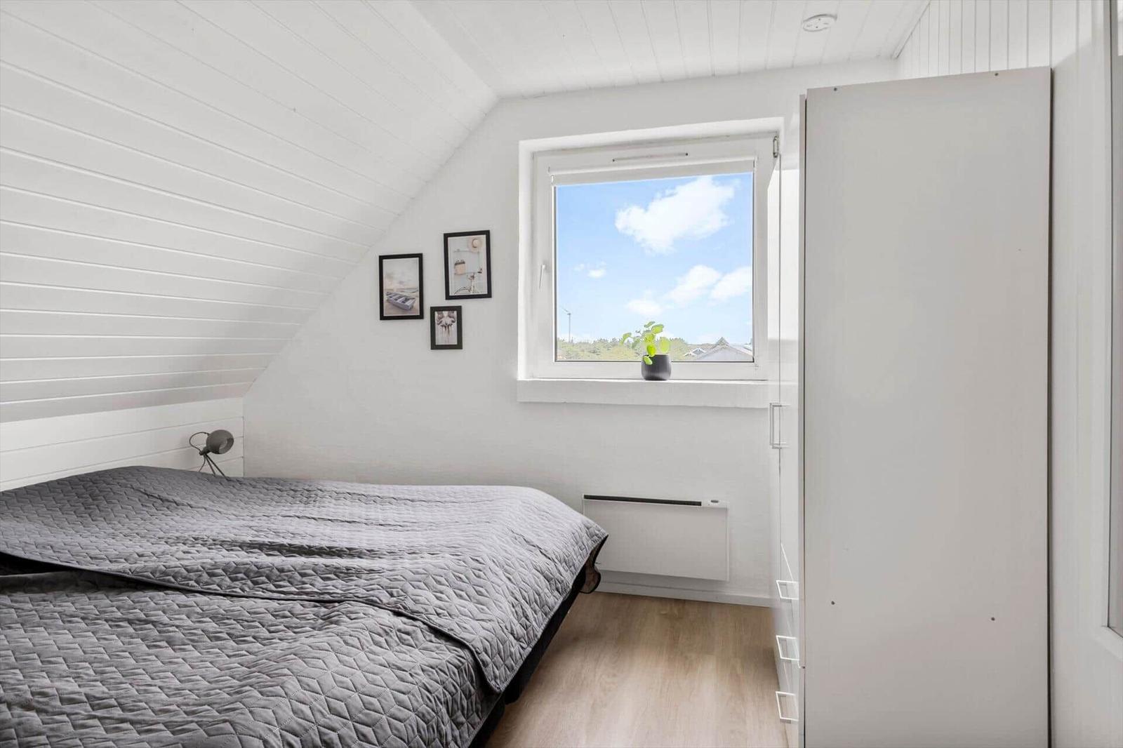 Bedroom with sloped ceiling, window, and bed with gray bedding.