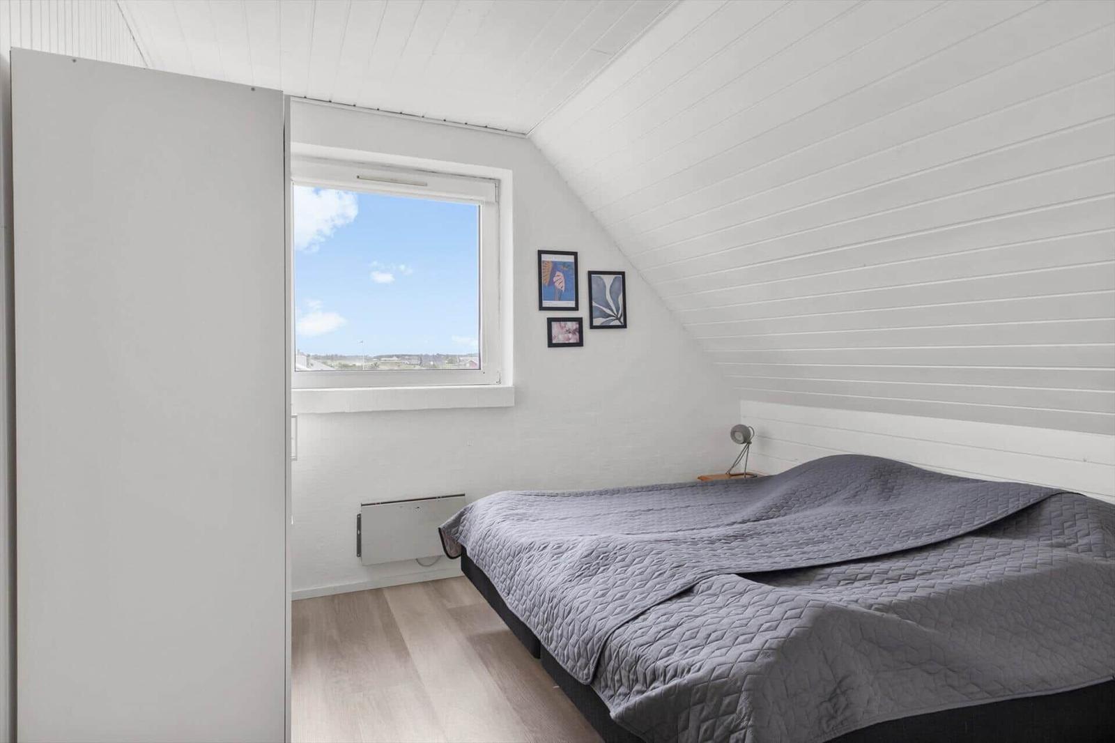 Bedroom with sloped ceiling, window, and bed with gray quilt.