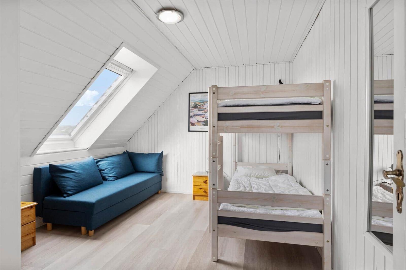 Room with bunk bed, sofa, and skylight. Wooden walls and floor.