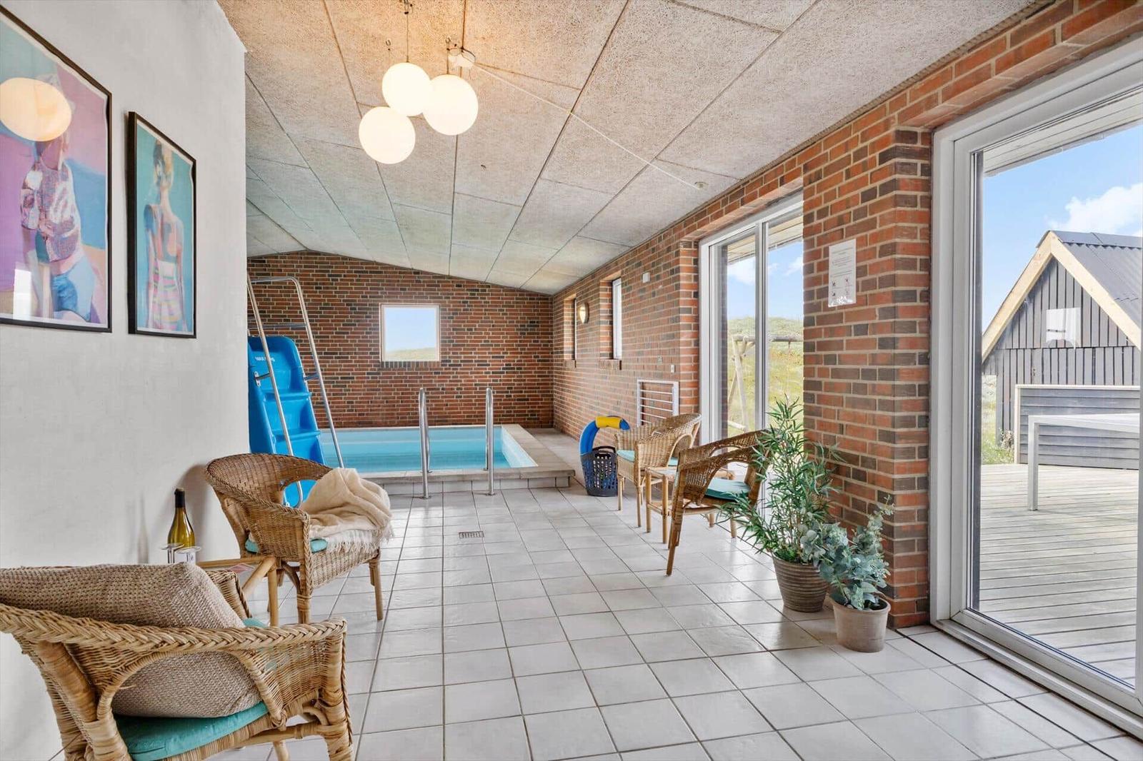 Indoor pool with seating and terrace. Brick wall and glass facade.