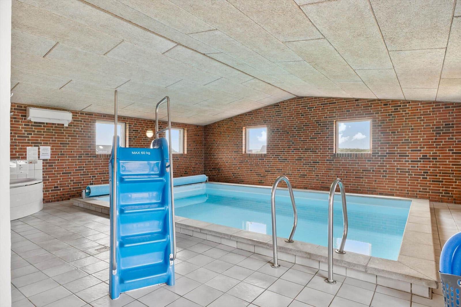 Indoor pool with blue ladder and metal steps, surrounded by brick walls and windows.