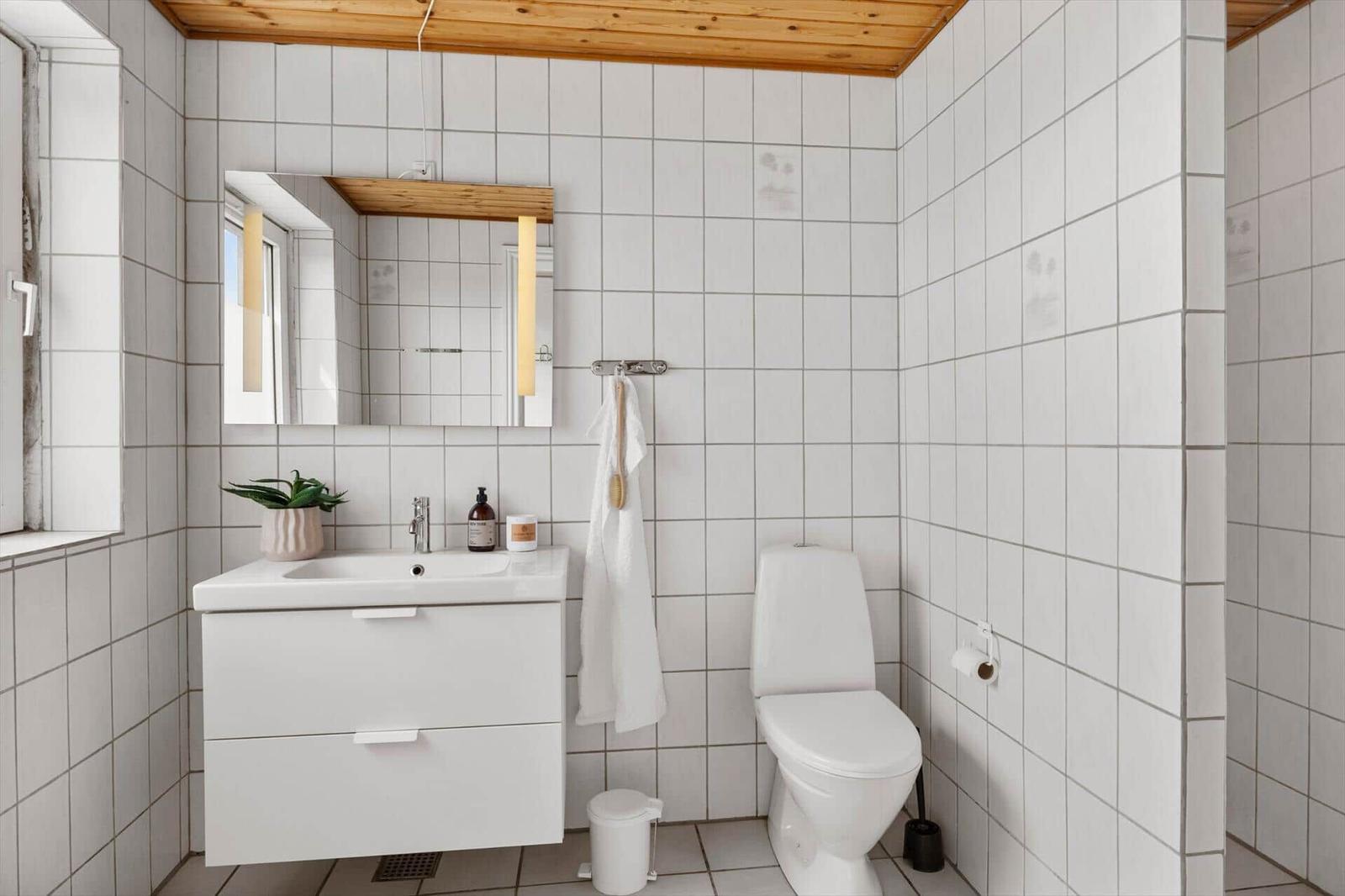 Bathroom with white tiled walls, sink, mirror, and toilet.