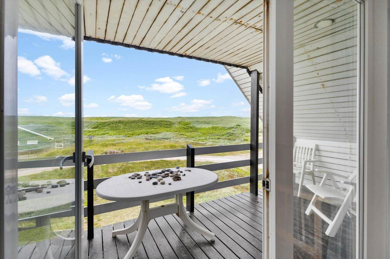 Deck with table and chairs, view of green fields under blue sky.