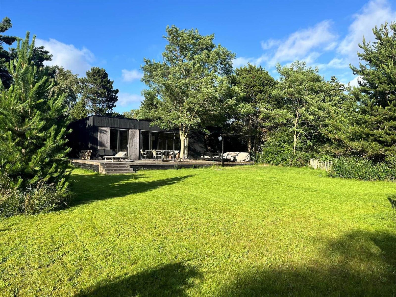 Moderne Villa mit Terrasse, Garten und Bäumen unter blauem Himmel.