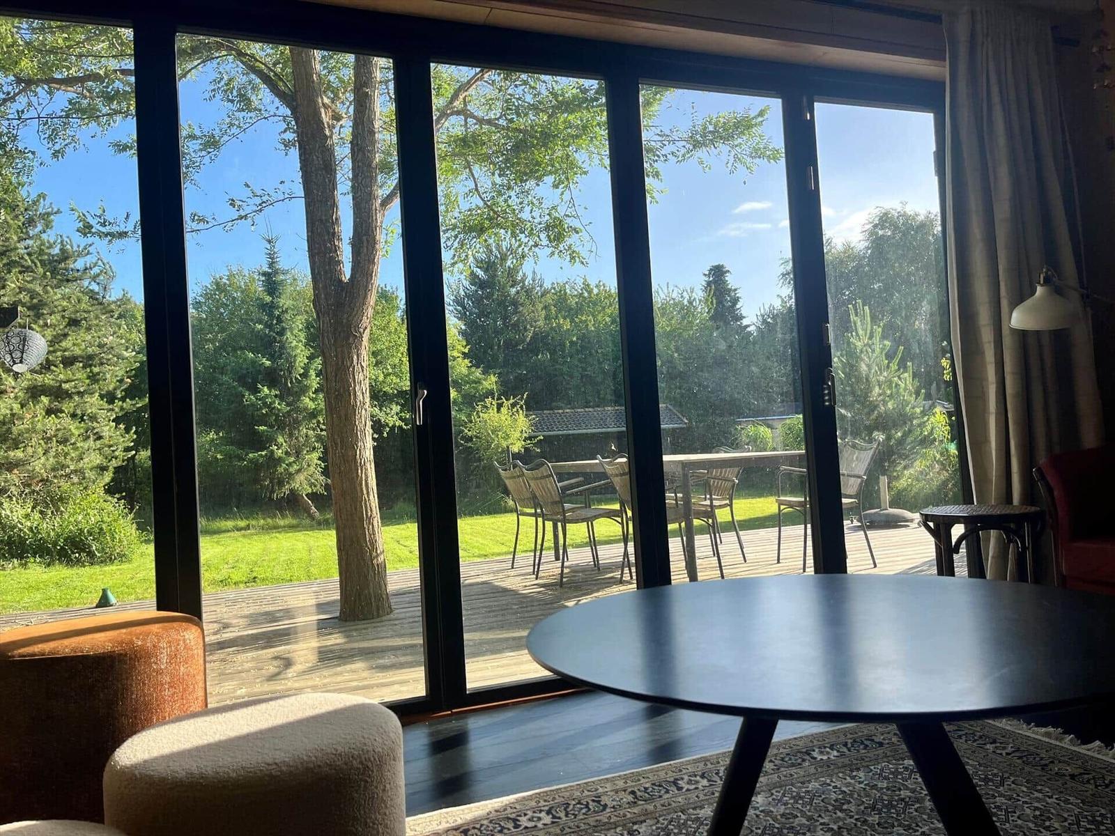 Große Glasfront mit Blick auf einen Garten mit Tisch und Stühlen.