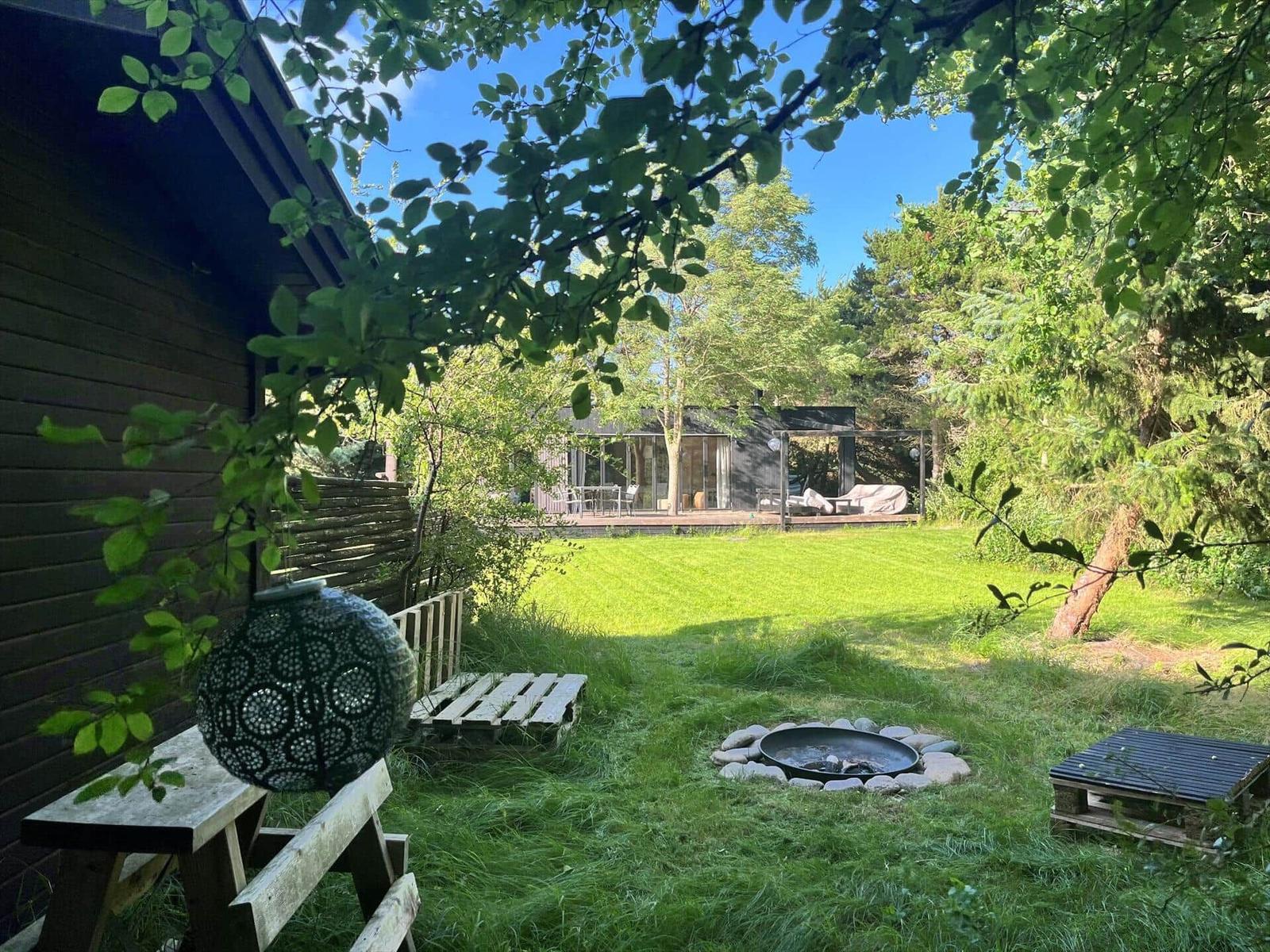 Grüner Garten mit Feuerkorb, Holzbank und Pavillon im Hintergrund.