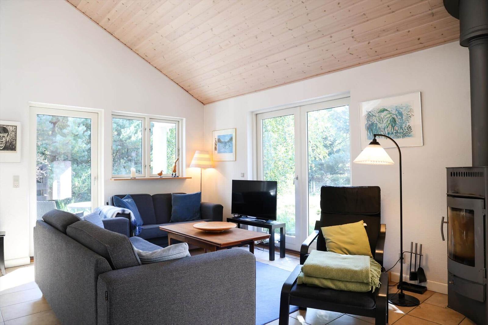Wohnzimmer mit Sofa, Sessel, Fernseher und Holzdecke.