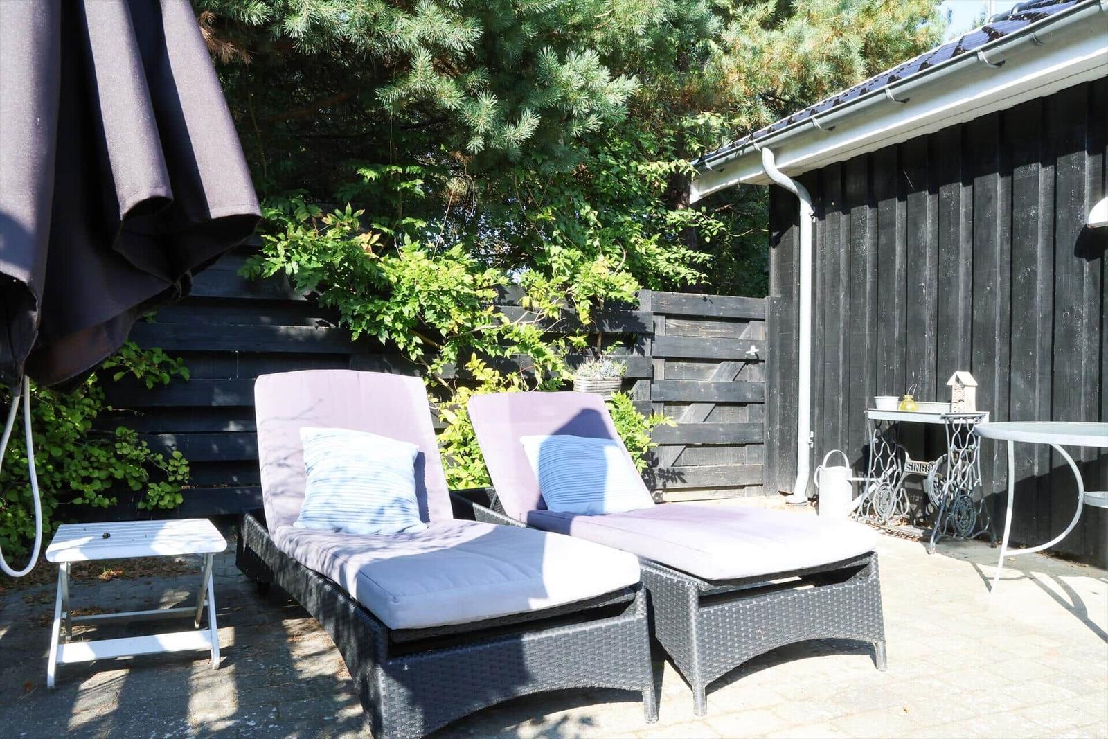Zwei Liegestühle mit Kissen stehen auf einer Terrasse neben einem geschlossenen Sonnenschirm.