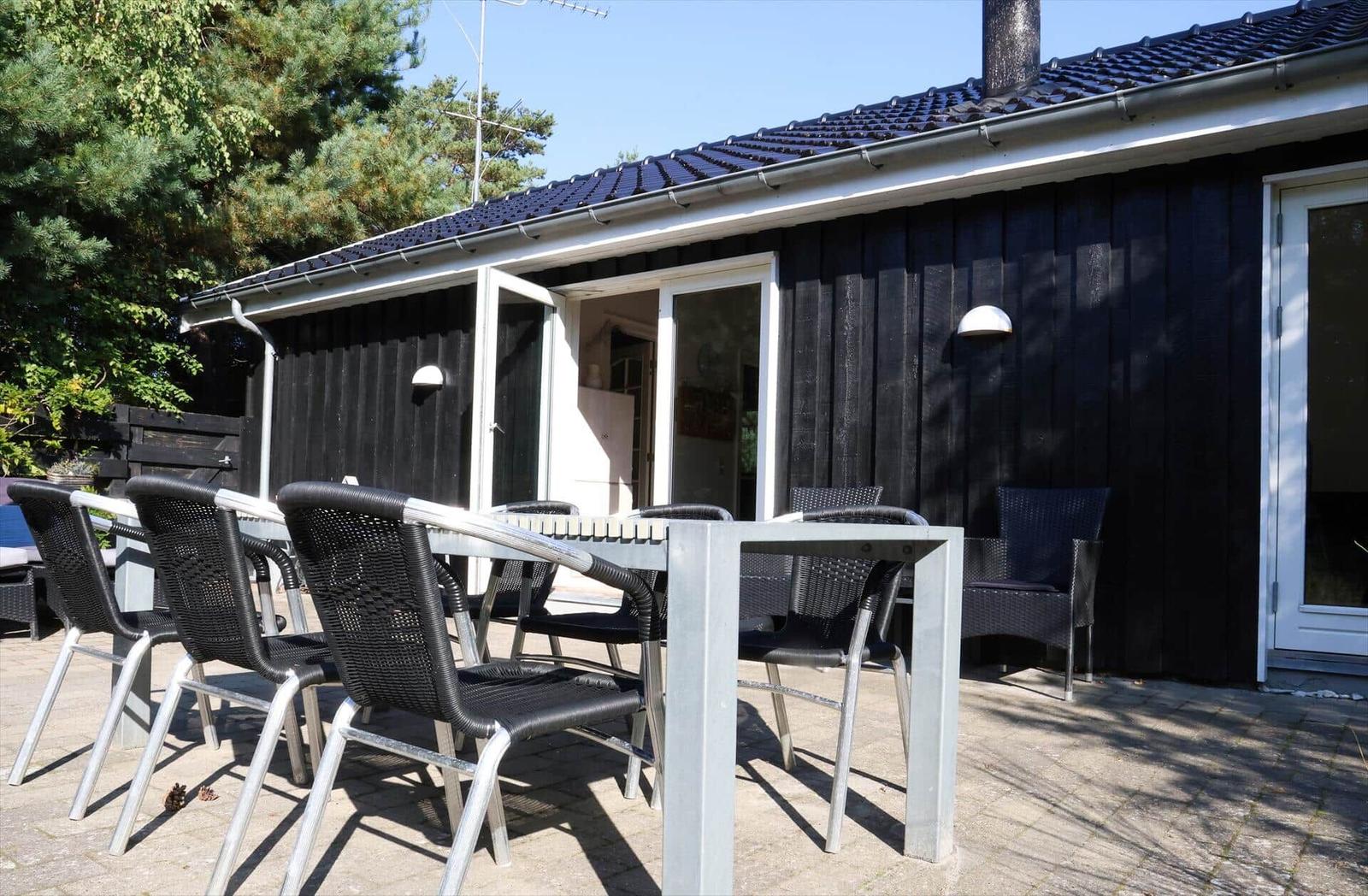 Terrasse mit Tisch und Stühlen vor einem Haus mit schwarzer Fassade und weißen Fensterrahmen.