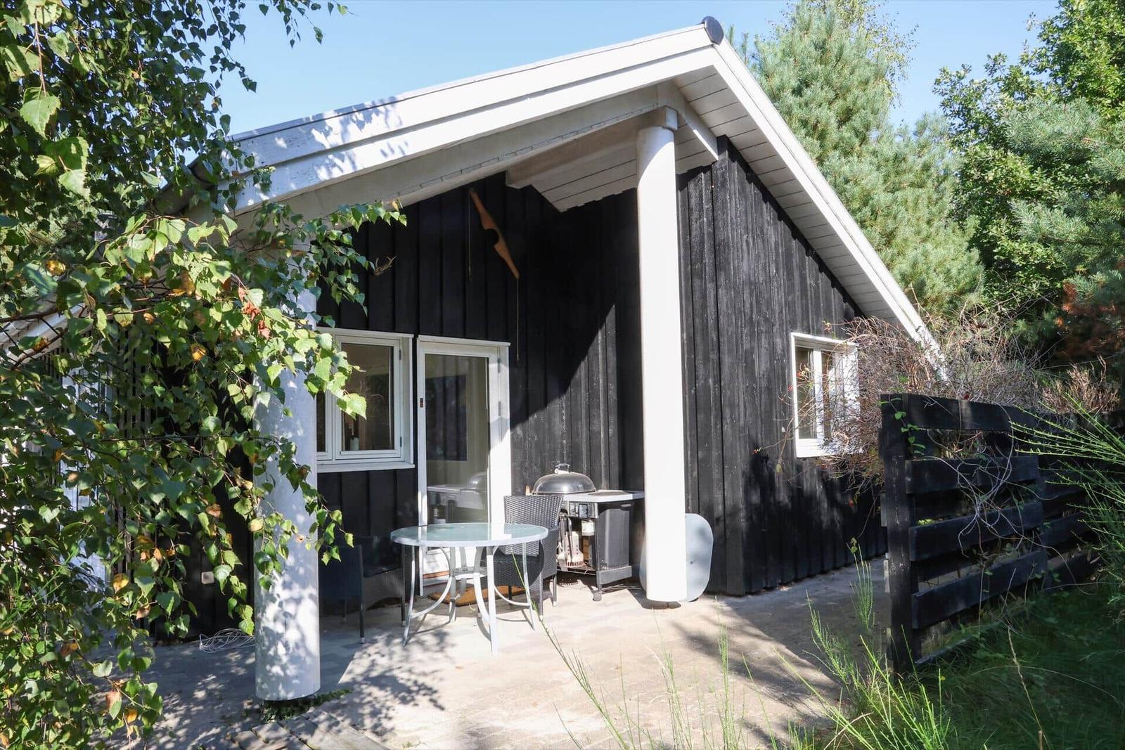 Schwarzes Holzhaus mit Terrasse, Grill und Garten. Fenster und Tür sind weiß.